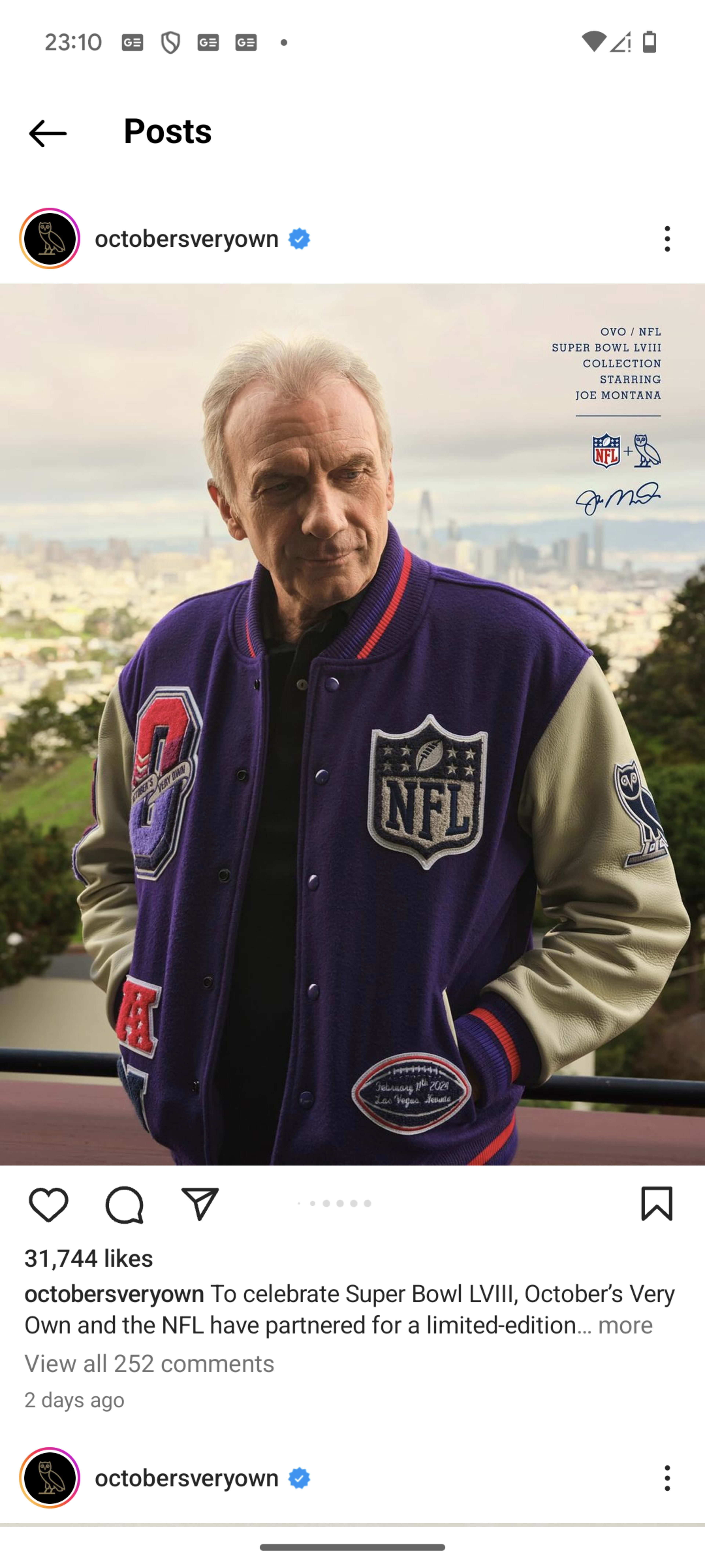 A man stands outside wearing a purple NFL varsity jacket, with a cityscape visible in the background.