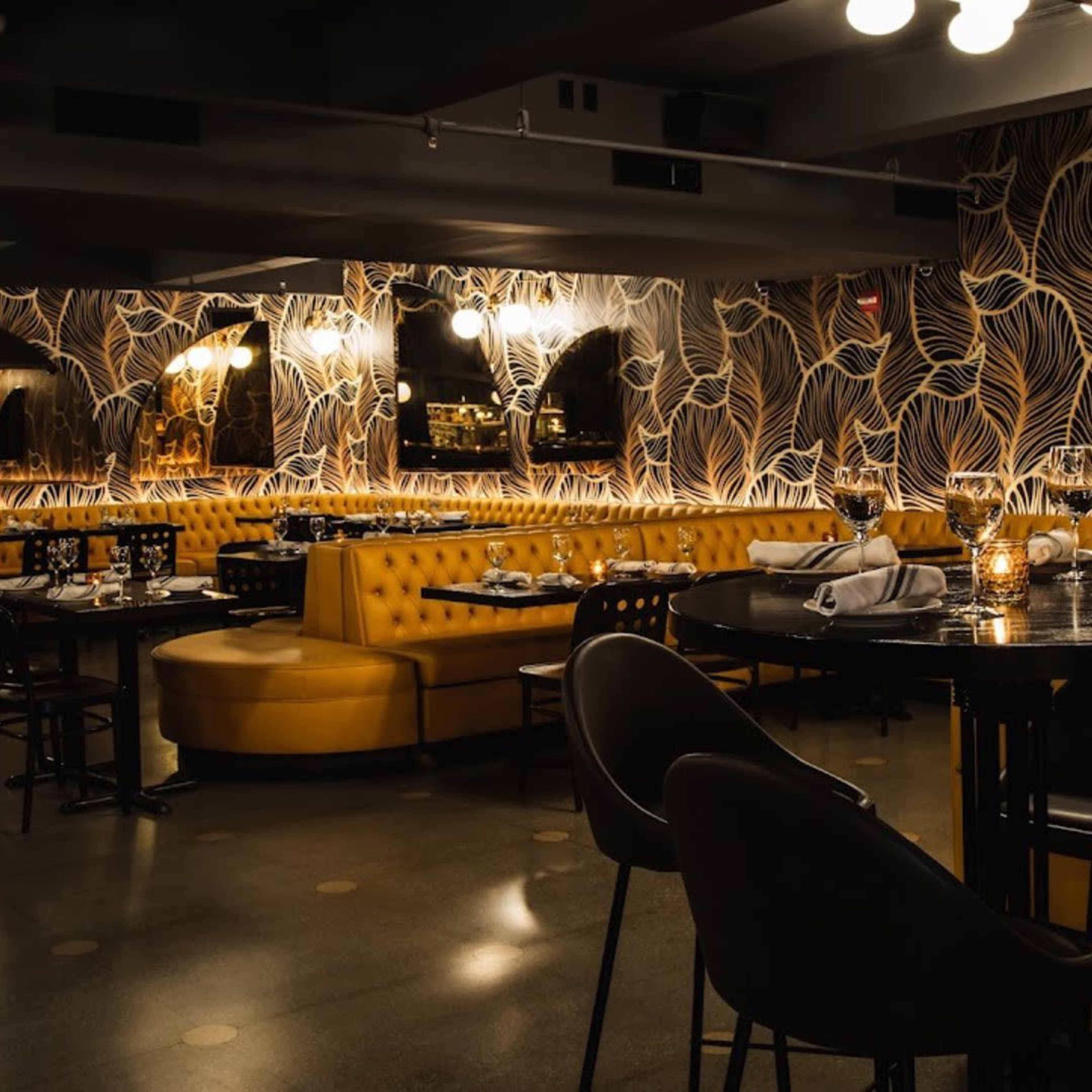 The image shows a modern restaurant interior with yellow upholstered seating, dark tables, and intricate floral wallpaper.