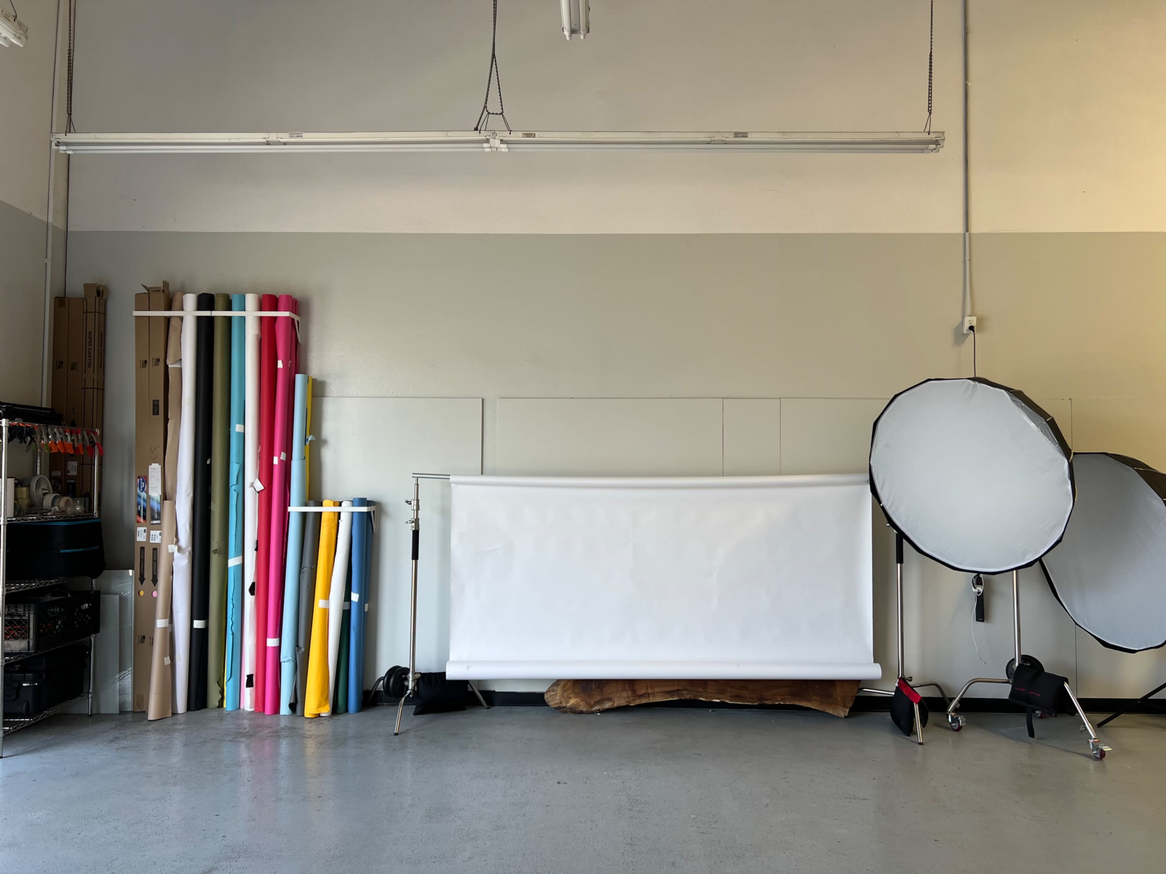 The image shows a photography studio with colorful backdrops neatly arranged on one side and a white backdrop setup with lighting equipment on the other side.