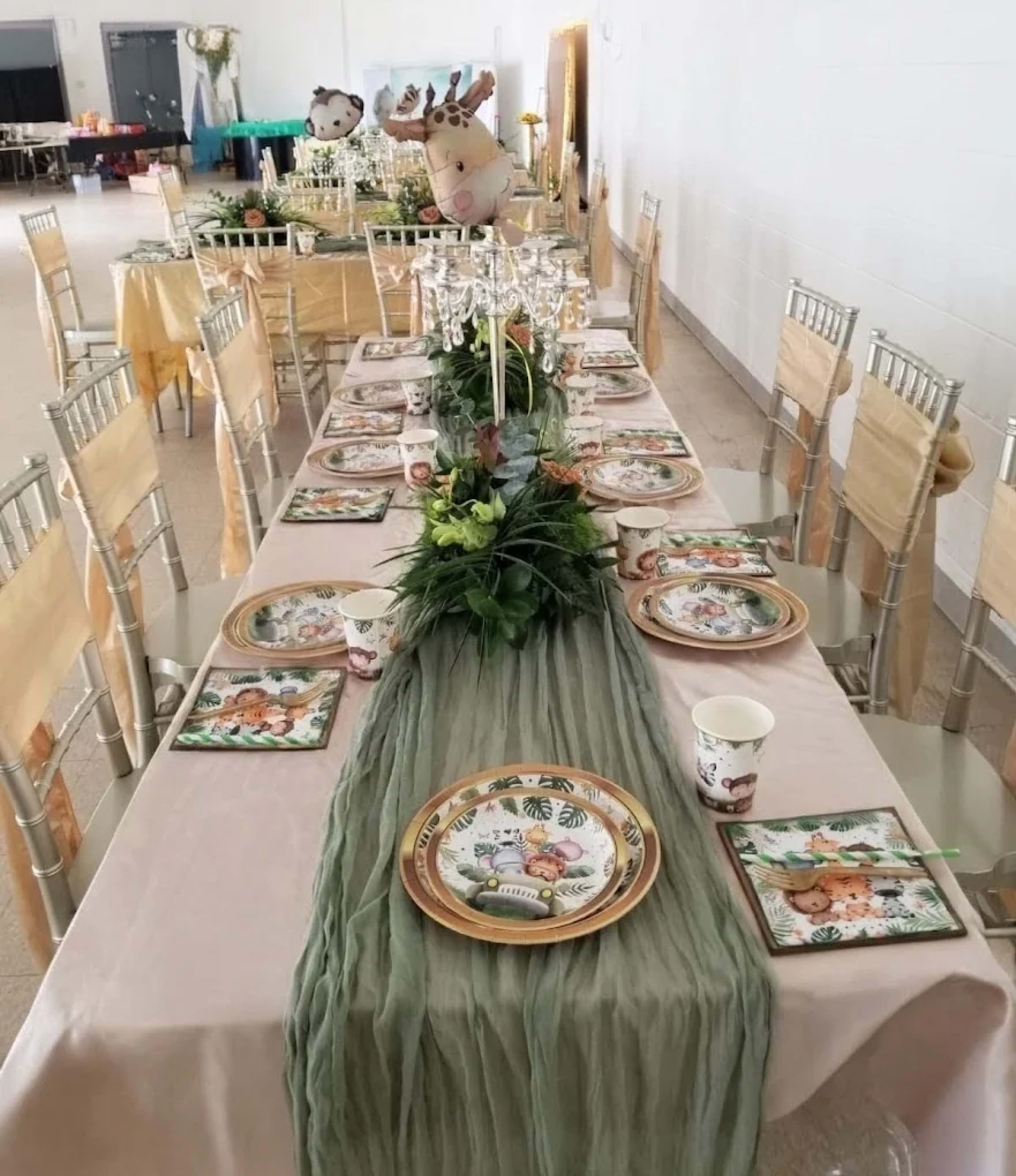 A long banquet table is elegantly set with patterned plates, a central floral arrangement, and decorative tableware in a spacious indoor venue.
