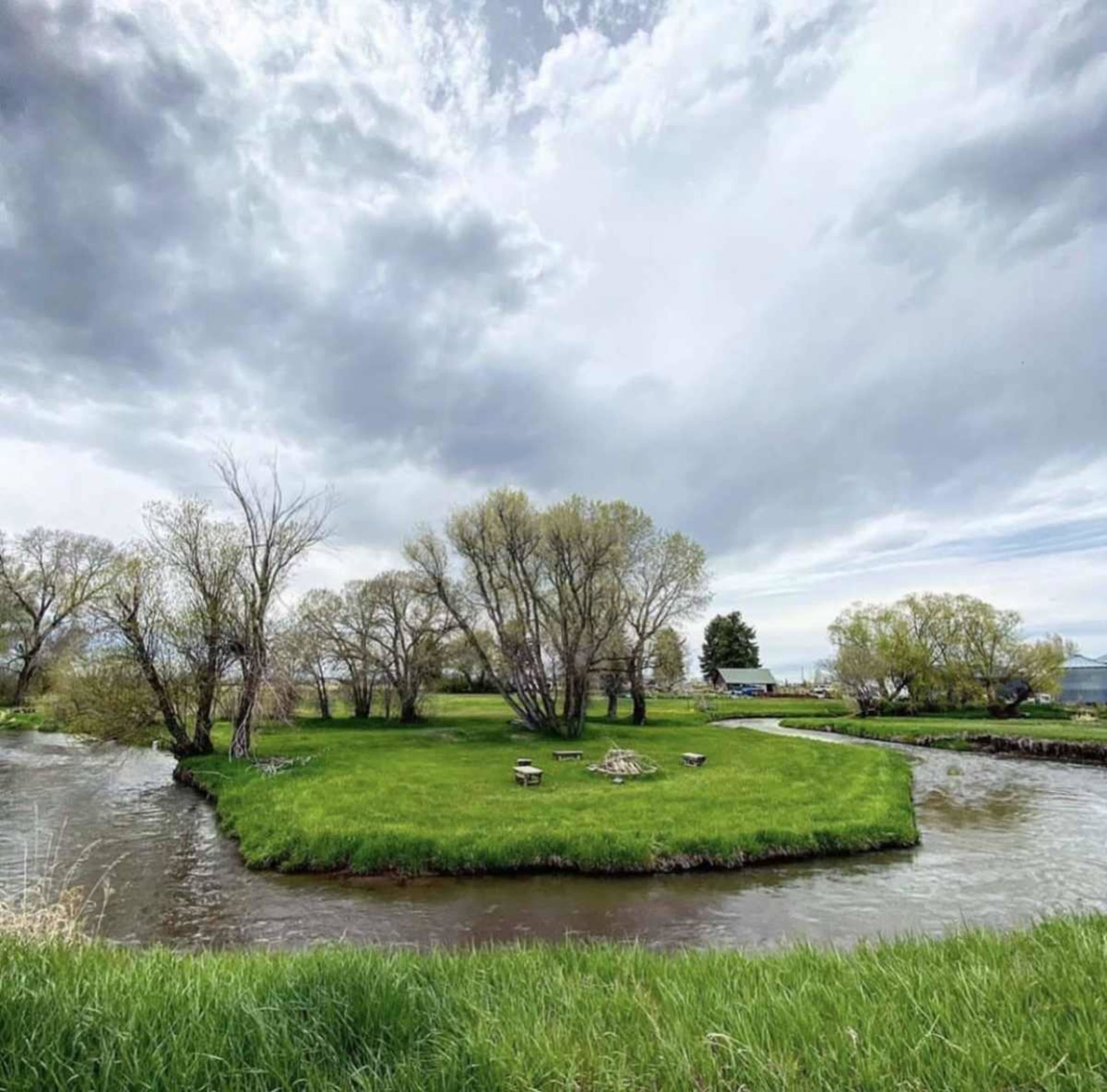 A grassy island with trees is surrounded by a winding river under a cloudy sky.