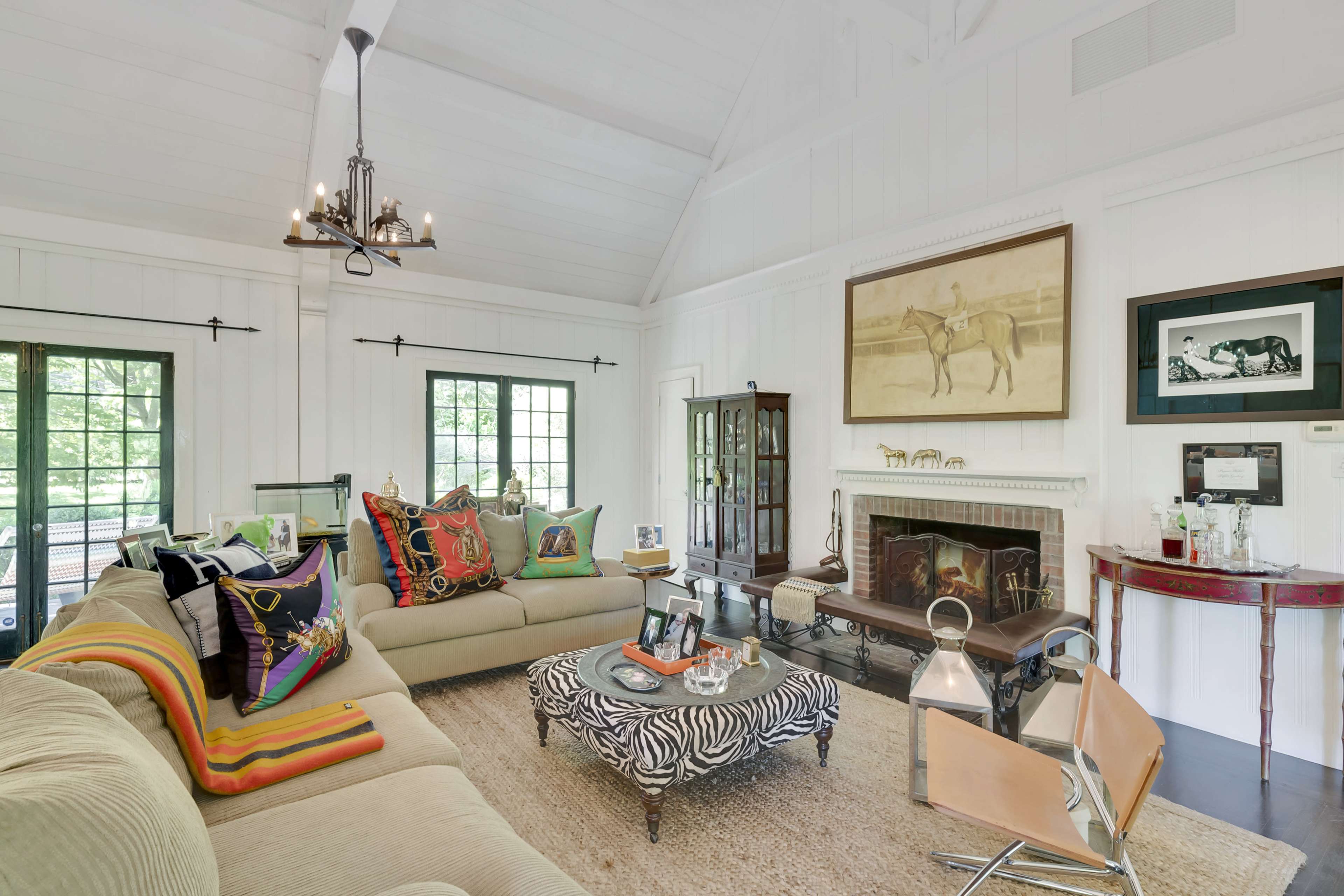 The living room features a large sectional sofa with colorful cushions, a zebra-patterned coffee table, and a fireplace surrounded by framed artworks.