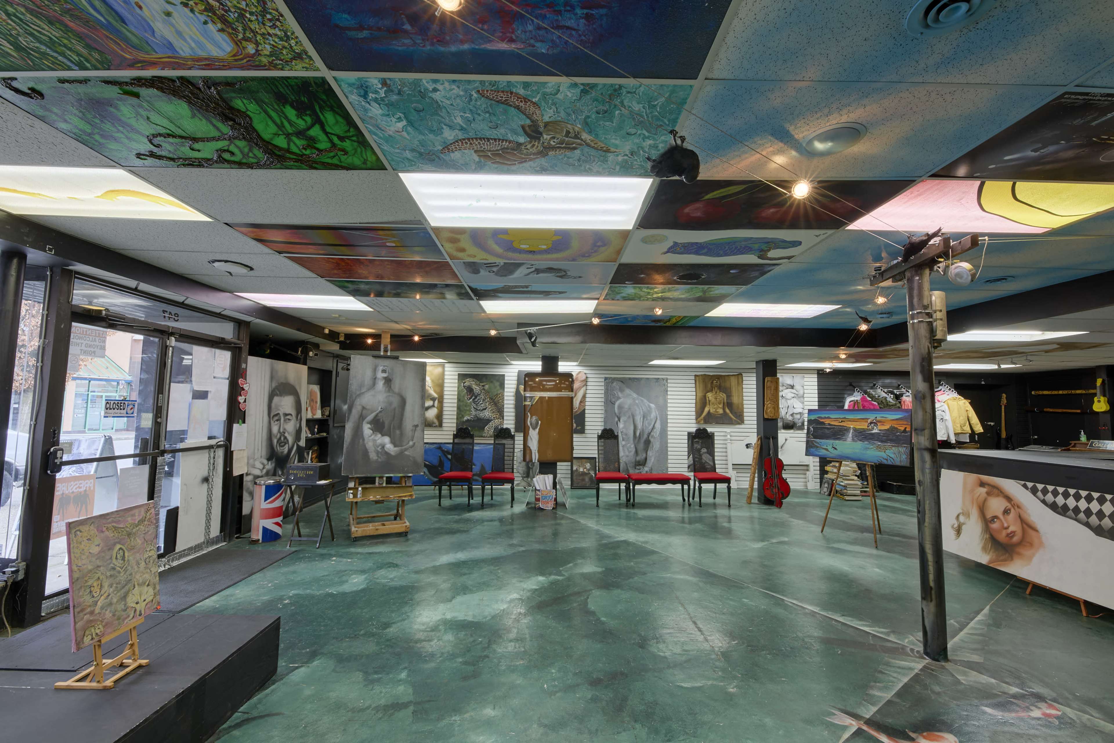 The image shows an art gallery with a colorful, mural-covered ceiling and various artworks displayed on the walls, including portraits and abstract pieces.