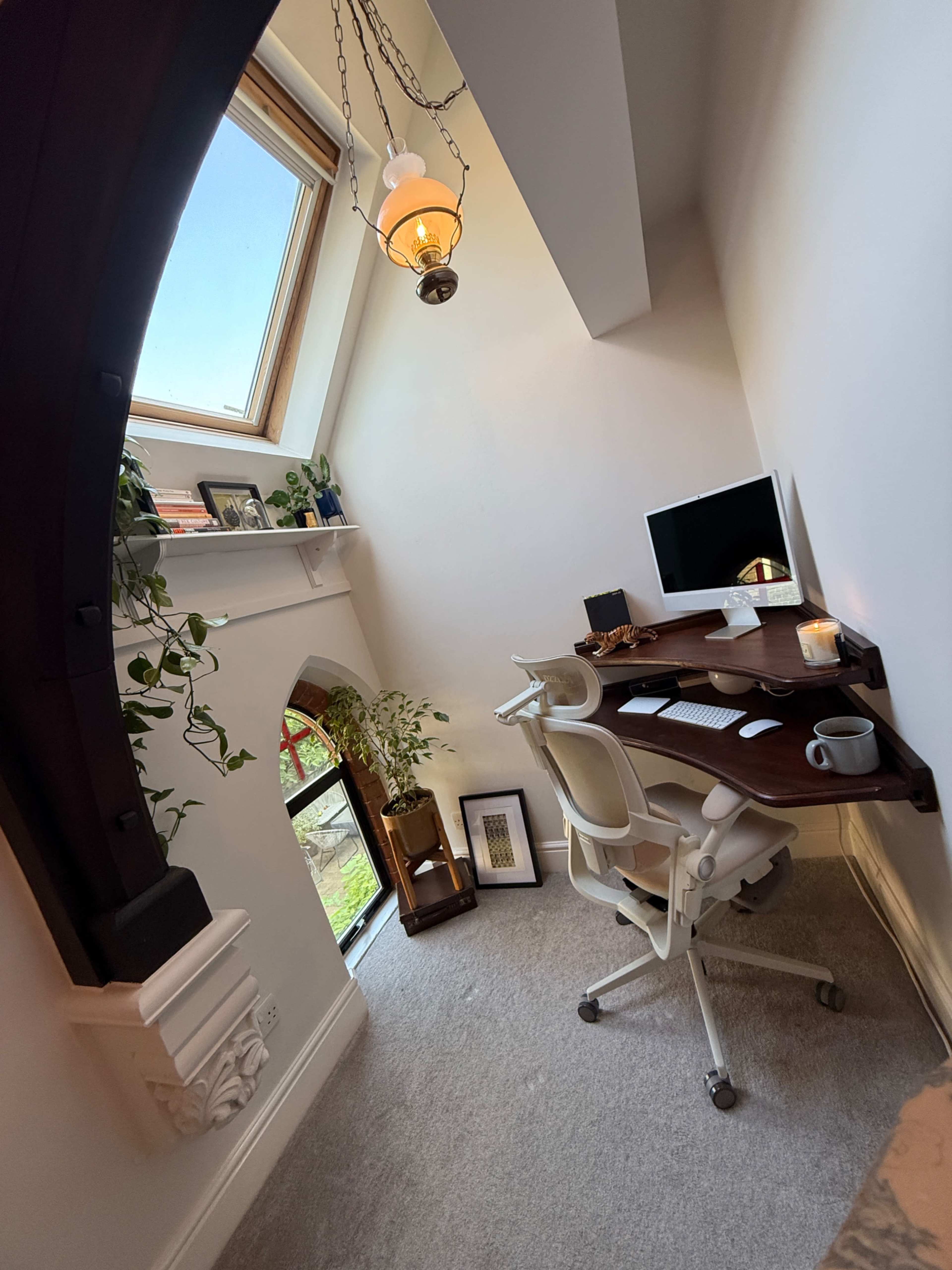 The image shows a cozy home office with a desk, computer, and decorative plants, all set under a slanted roof with a skylight.