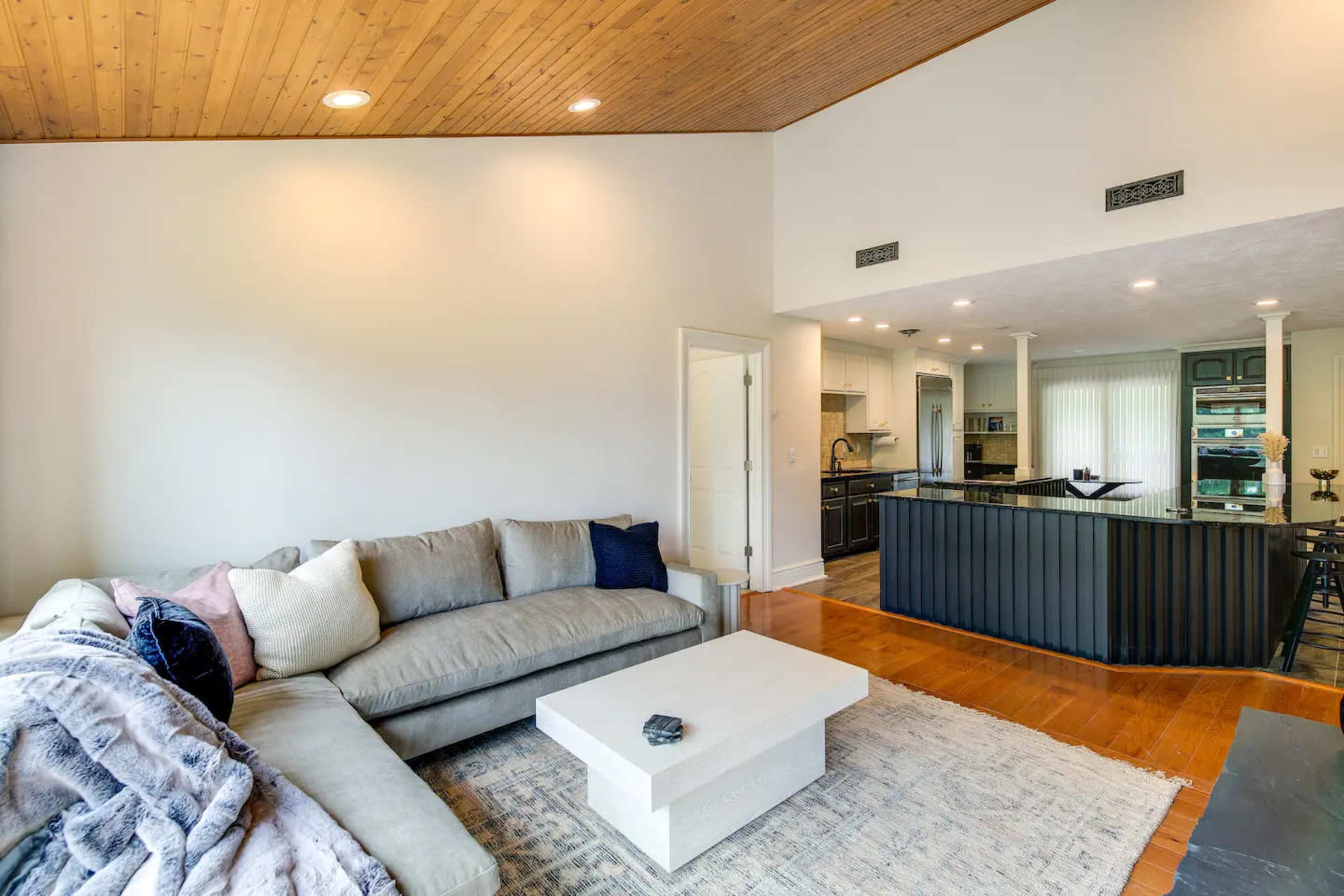A modern living room with a sectional sofa, a coffee table, and a kitchen area in the background.