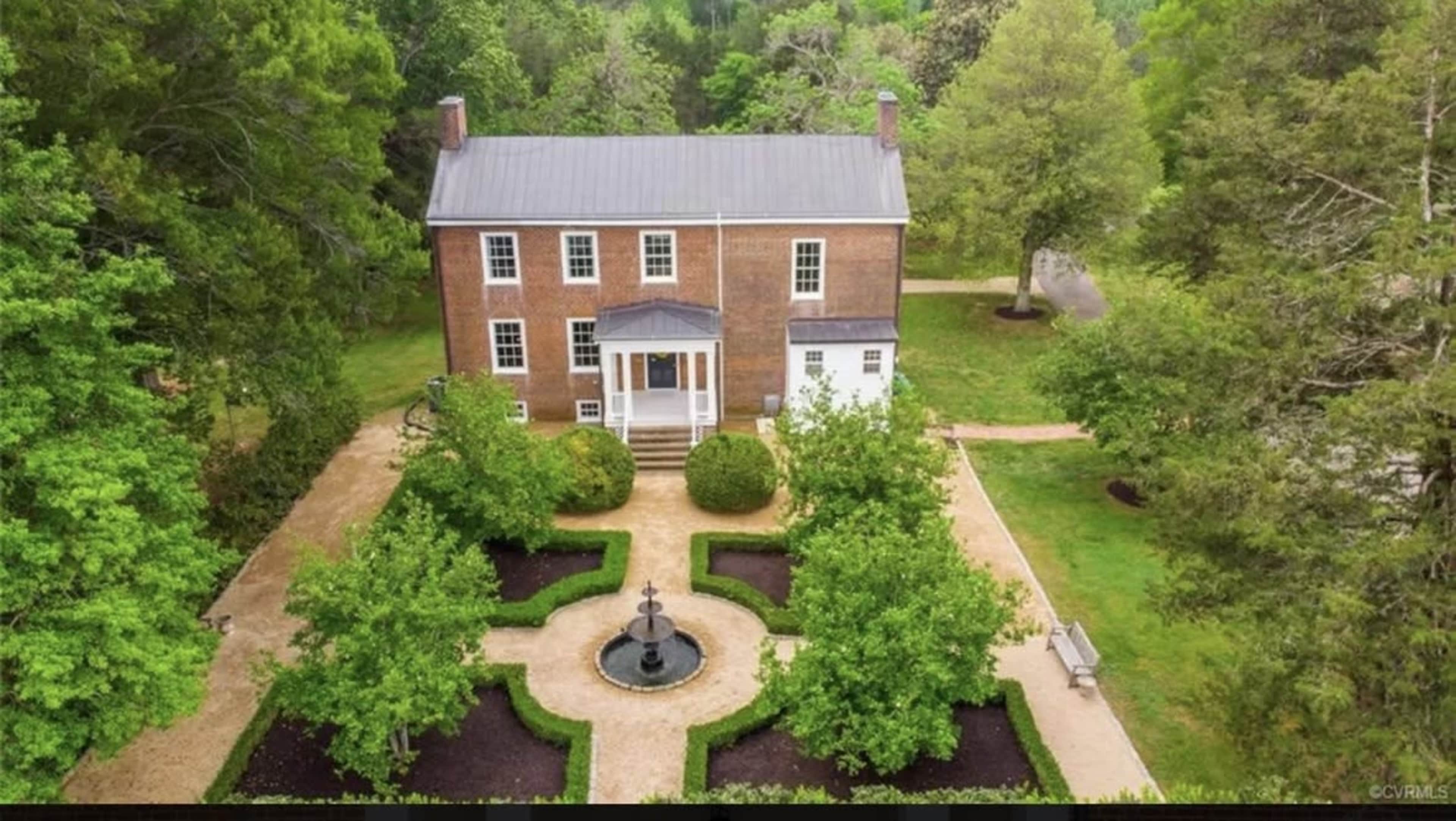 A two-story brick house surrounded by a landscaped garden featuring a central fountain and symmetrical pathways.