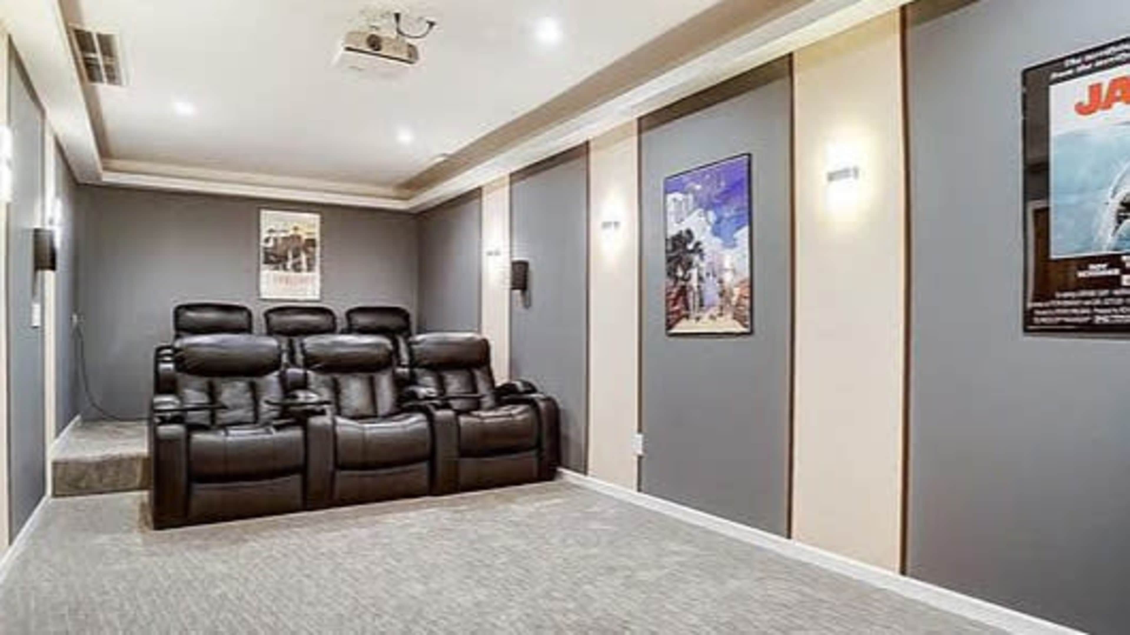 The image shows a home theater with plush black reclining chairs, movie posters on the walls, and overhead lighting.