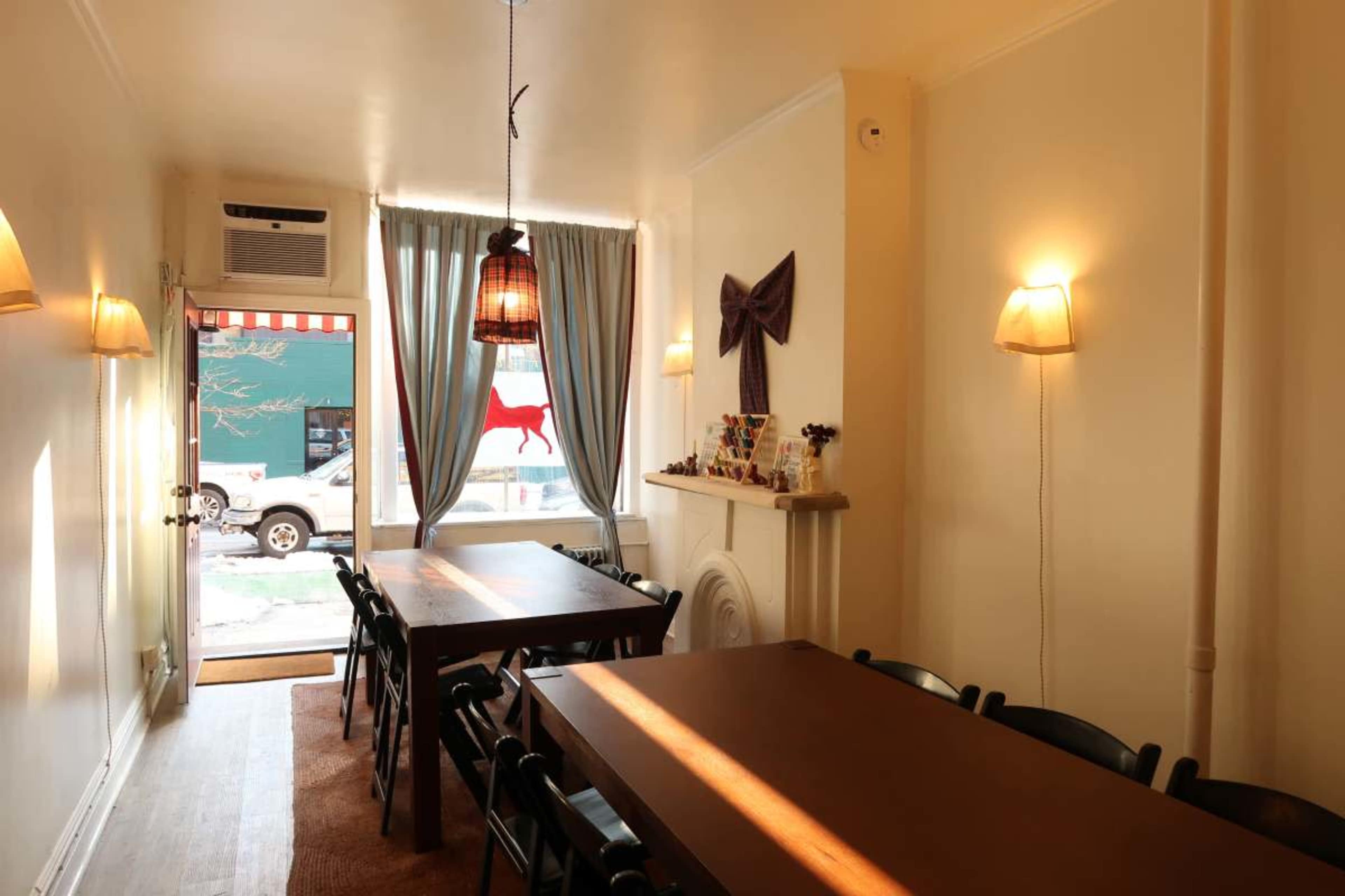 The image shows a cozy interior of a cafe with two wooden tables, chairs, and soft lighting from wall sconces.