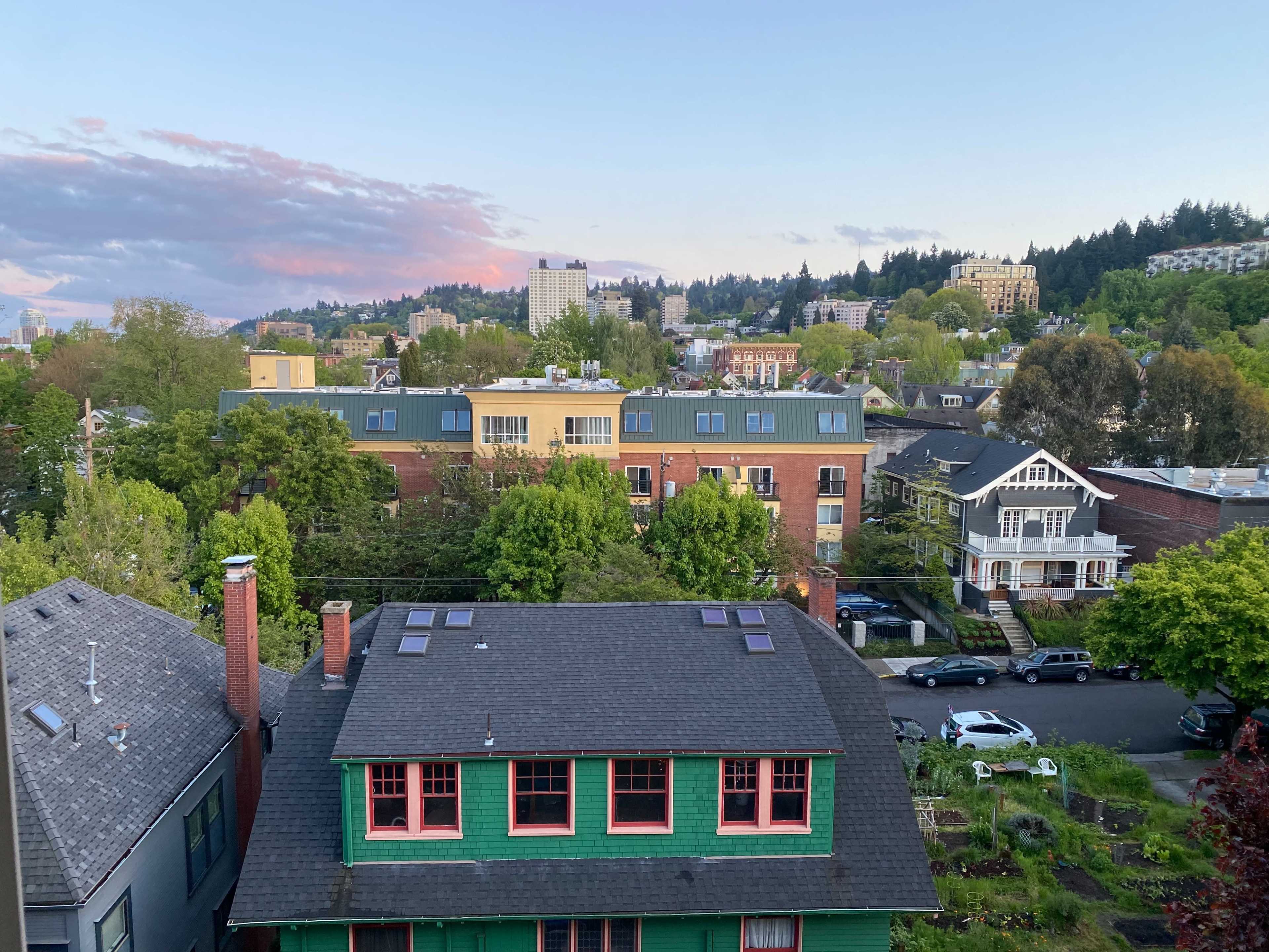 Aerial view of a neighborhood featuring a mix of residential buildings with trees and distant hills under a twilight sky.