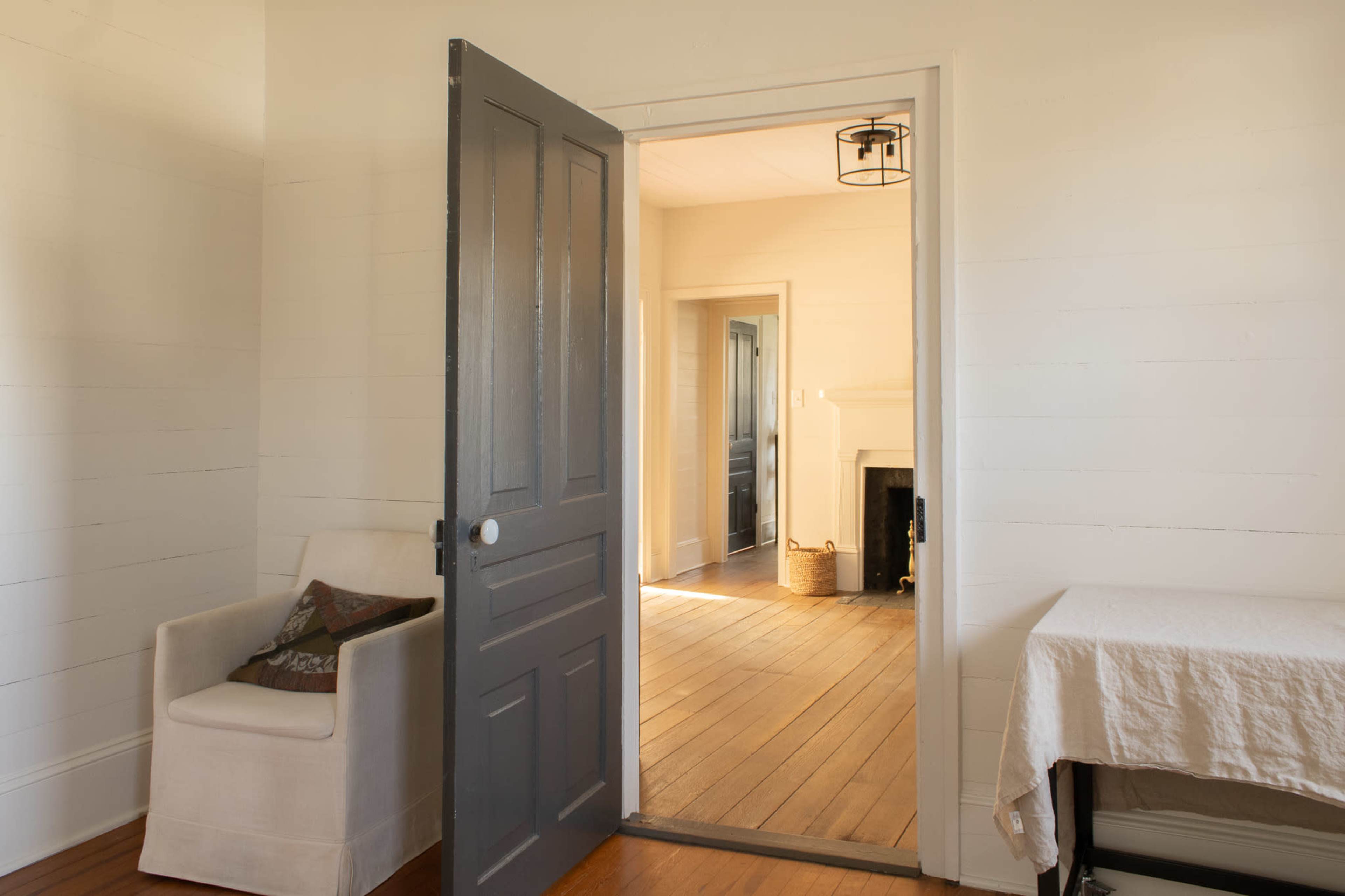 An open gray door leads into a light-filled room with wooden floors and a fireplace.