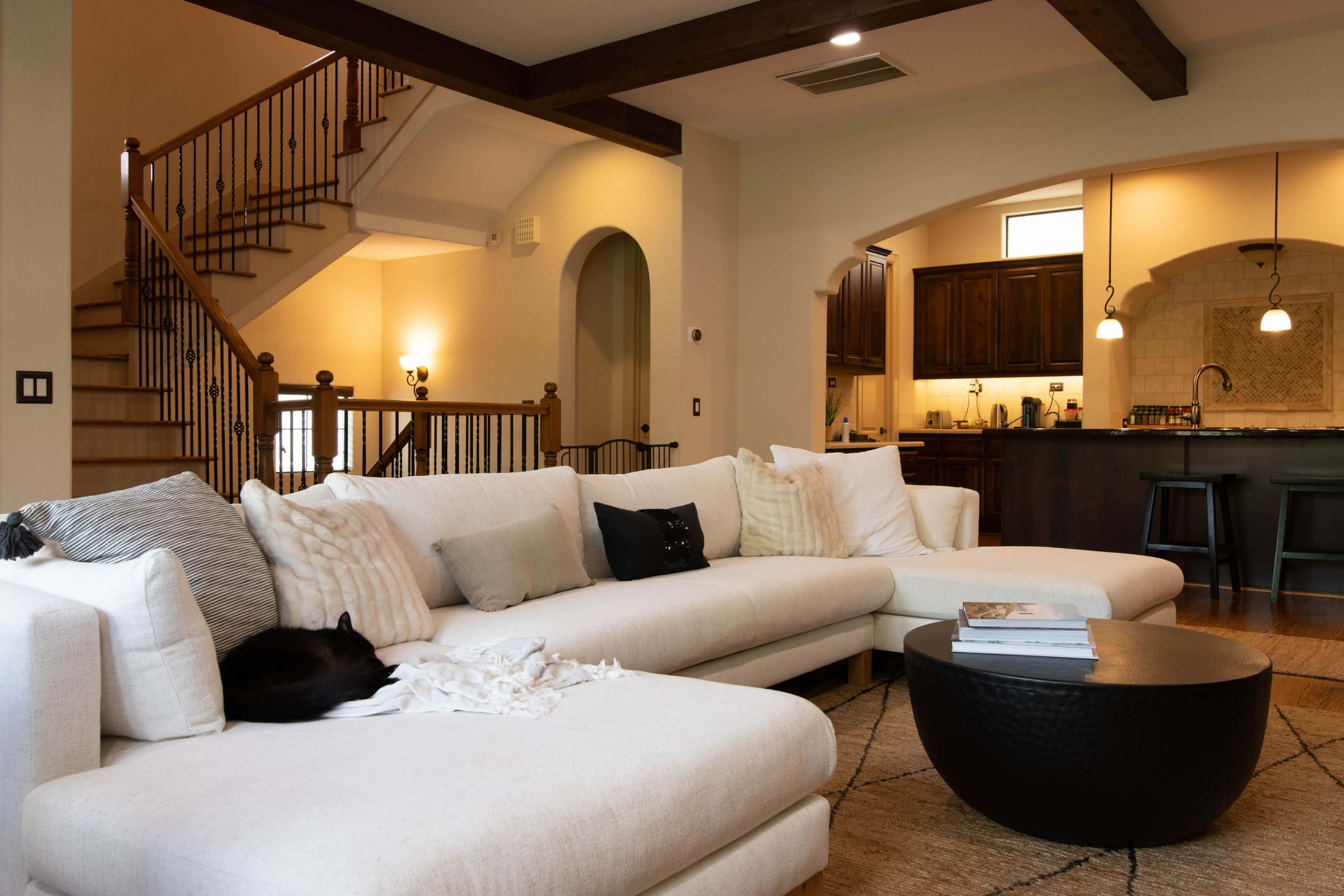 A modern living room features a large sectional couch, a round coffee table, and a view of a staircase leading to an upper level.