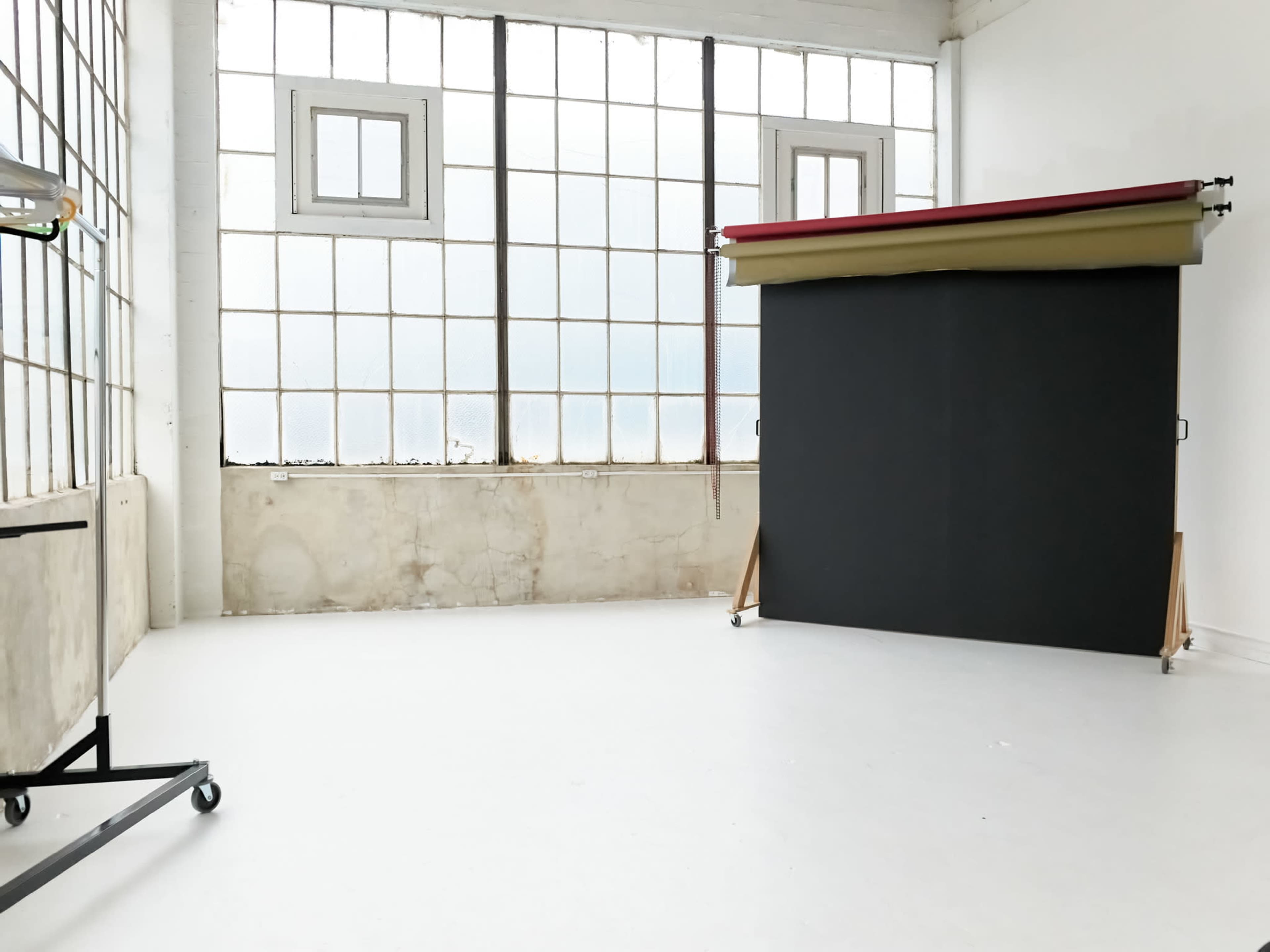The image shows a spacious, well-lit studio with large windows, a backdrop stand holding three different colored backdrops, and a clean white floor.