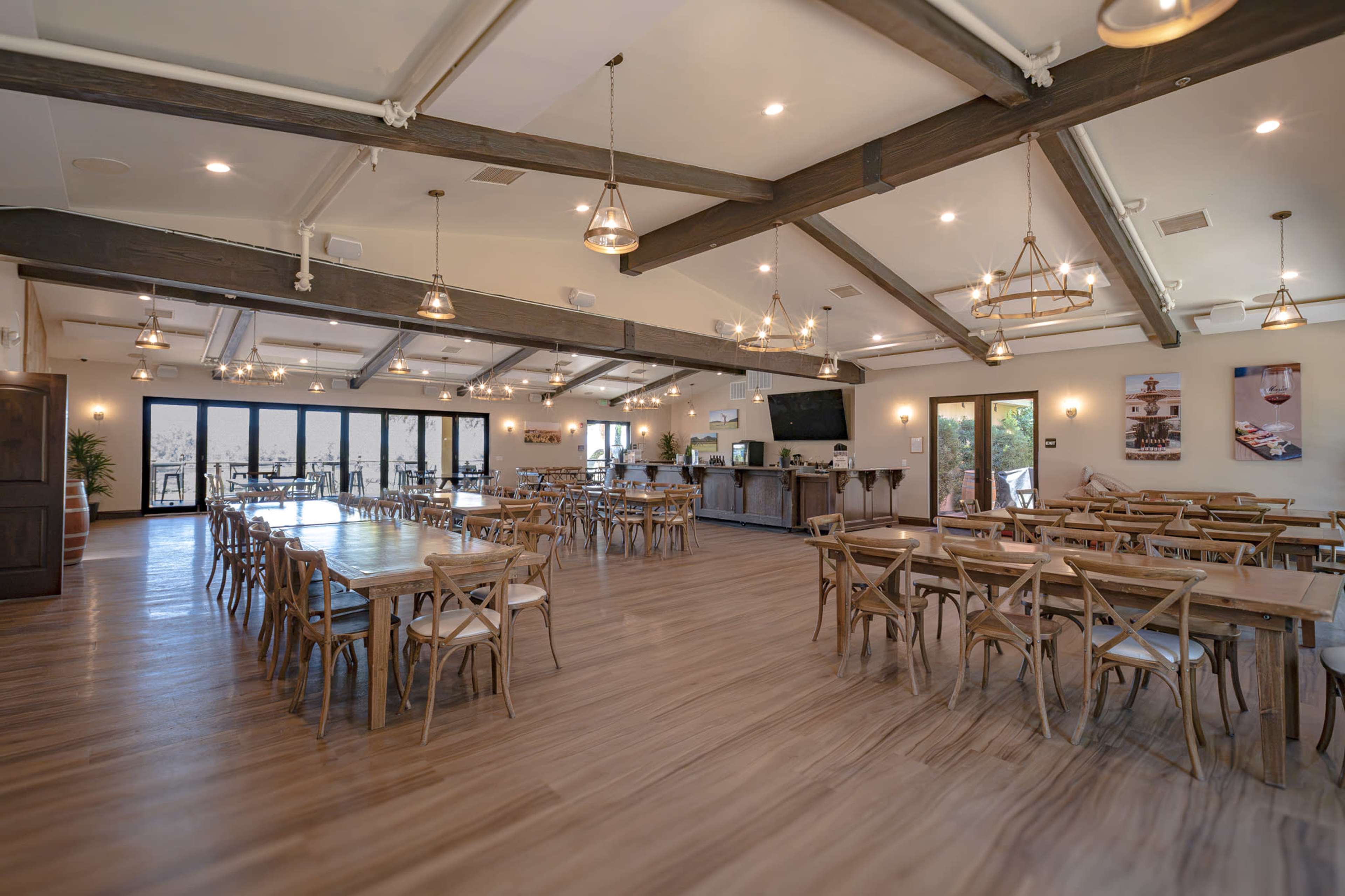 The image shows a spacious dining area with wooden tables and chairs, large windows, and pendant lighting.