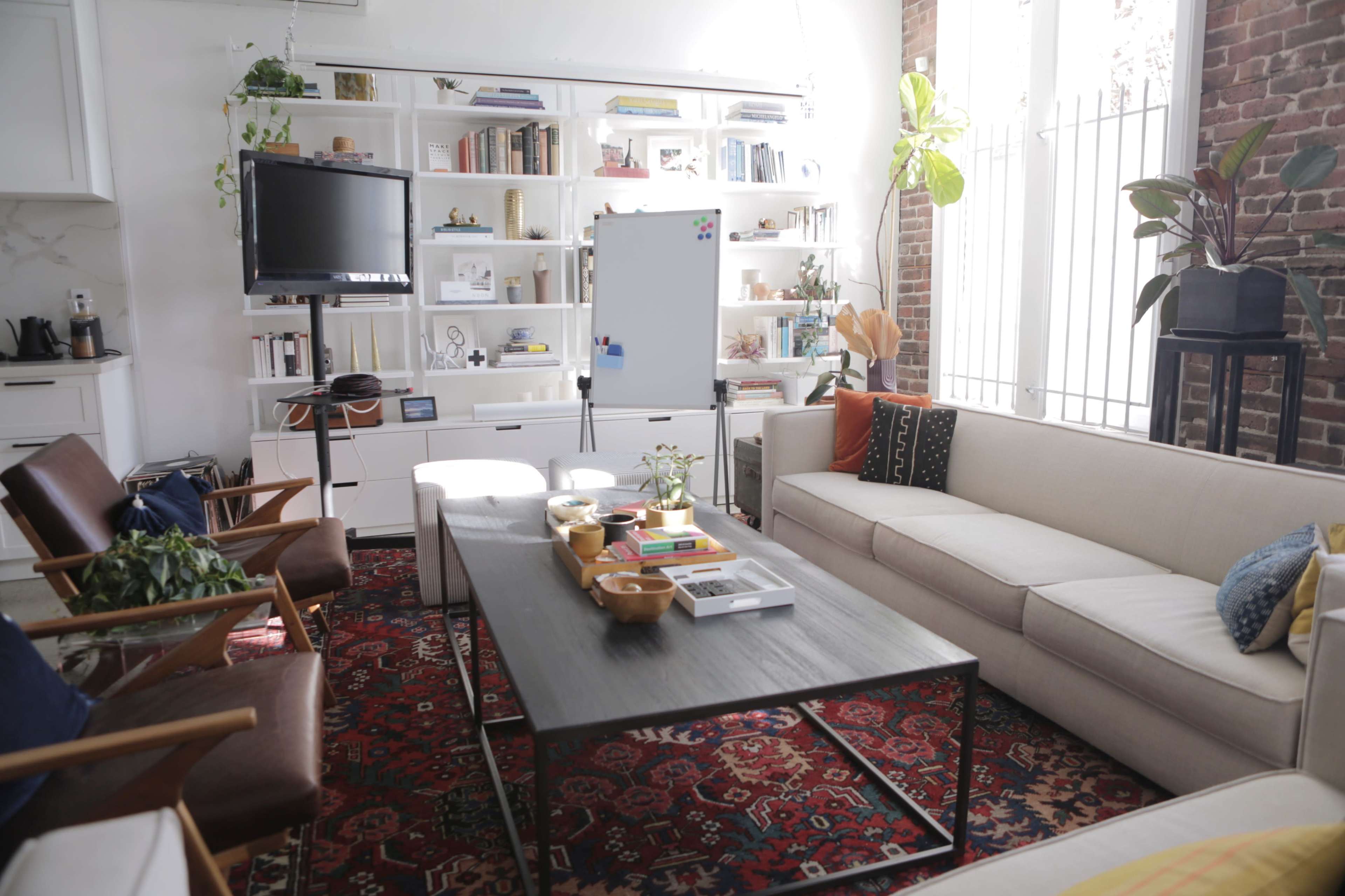 A cozy living area with a beige sofa, a dark coffee table, and a bookshelf filled with books and decorative items, all set against a backdrop of exposed brick walls.
