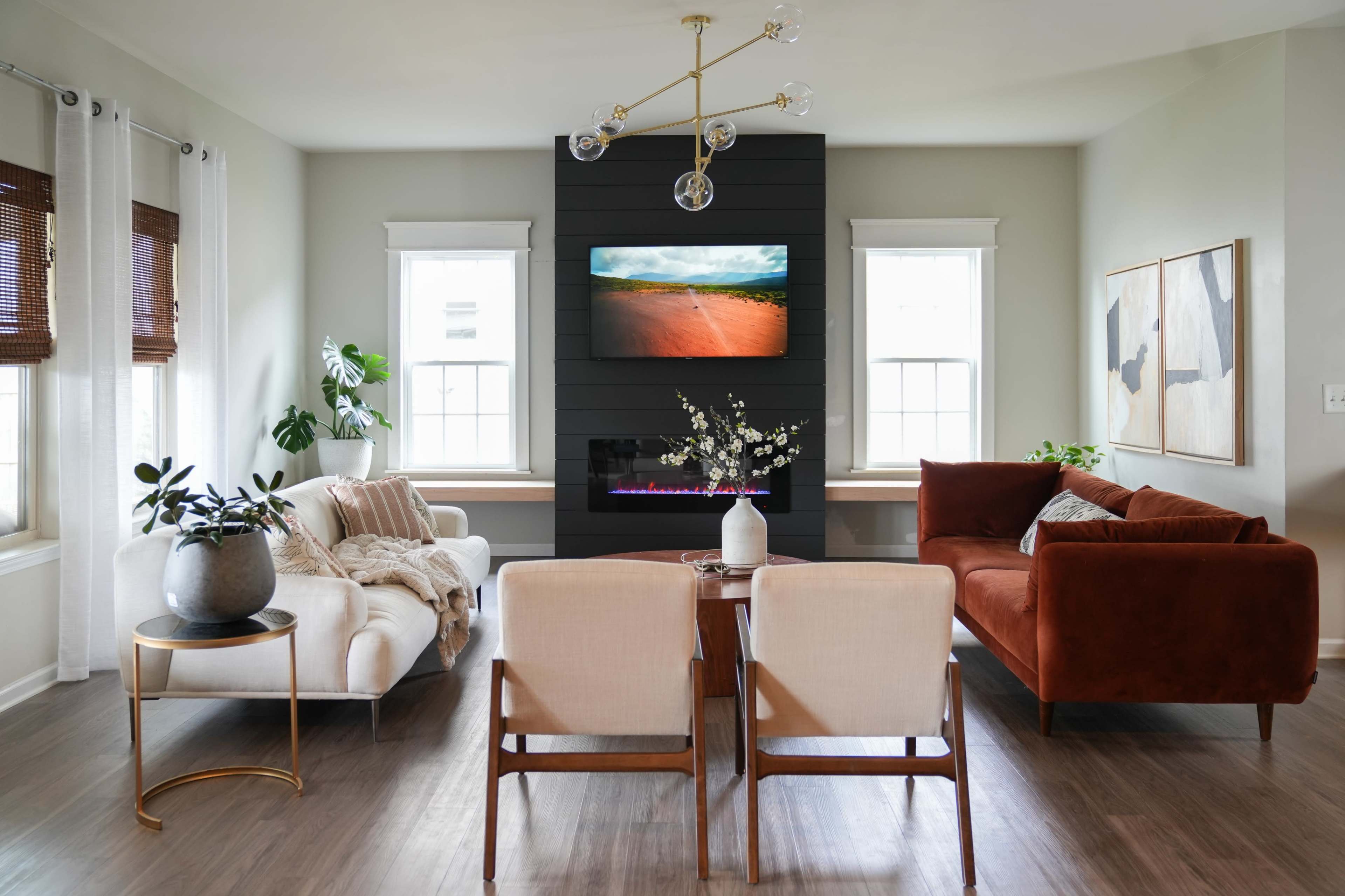 A modern living room features a dark accent wall with a mounted TV, two sofas, a coffee table, and large windows letting in natural light.