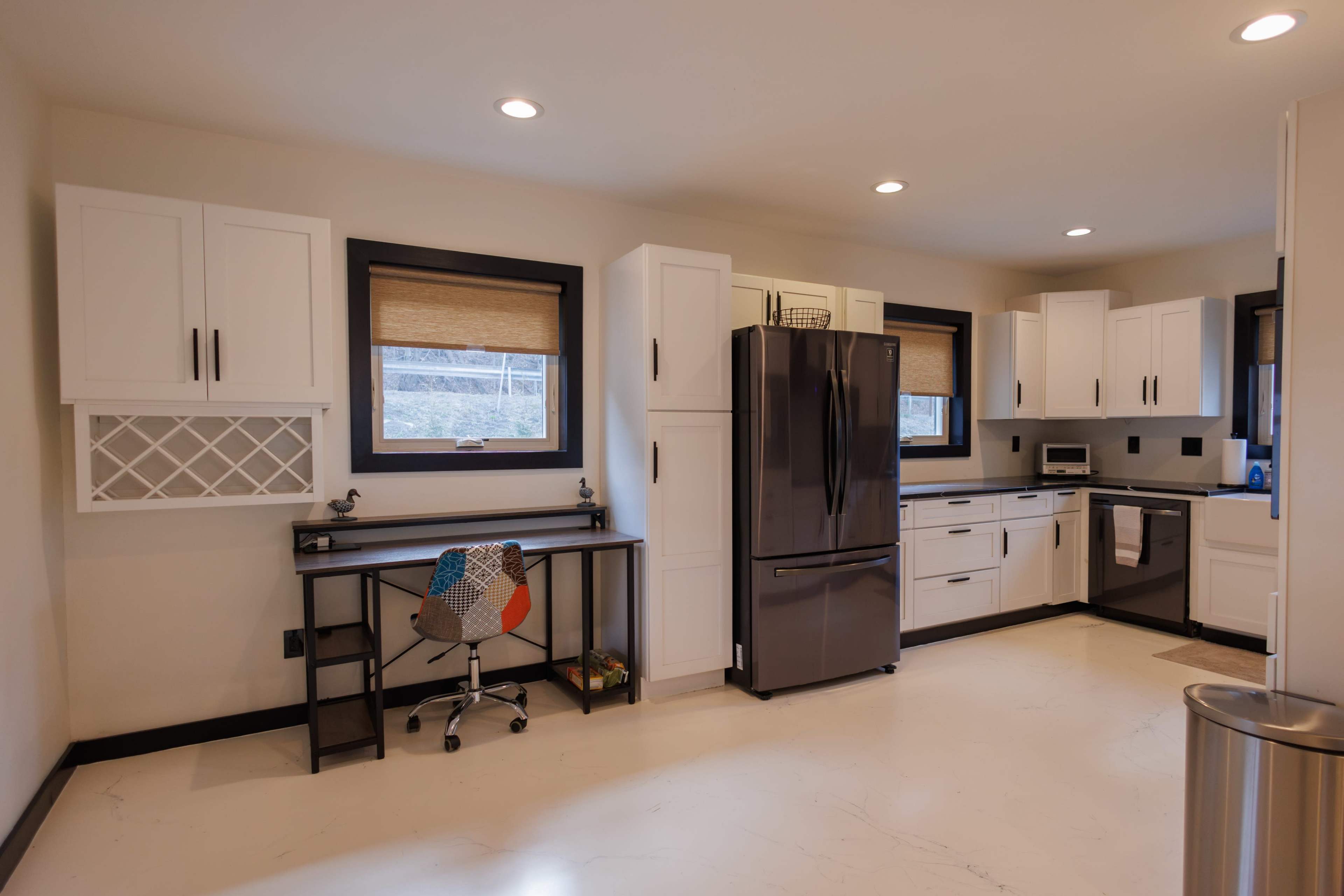 The kitchen features white cabinetry, a black refrigerator, and a workspace with a desk and chair.