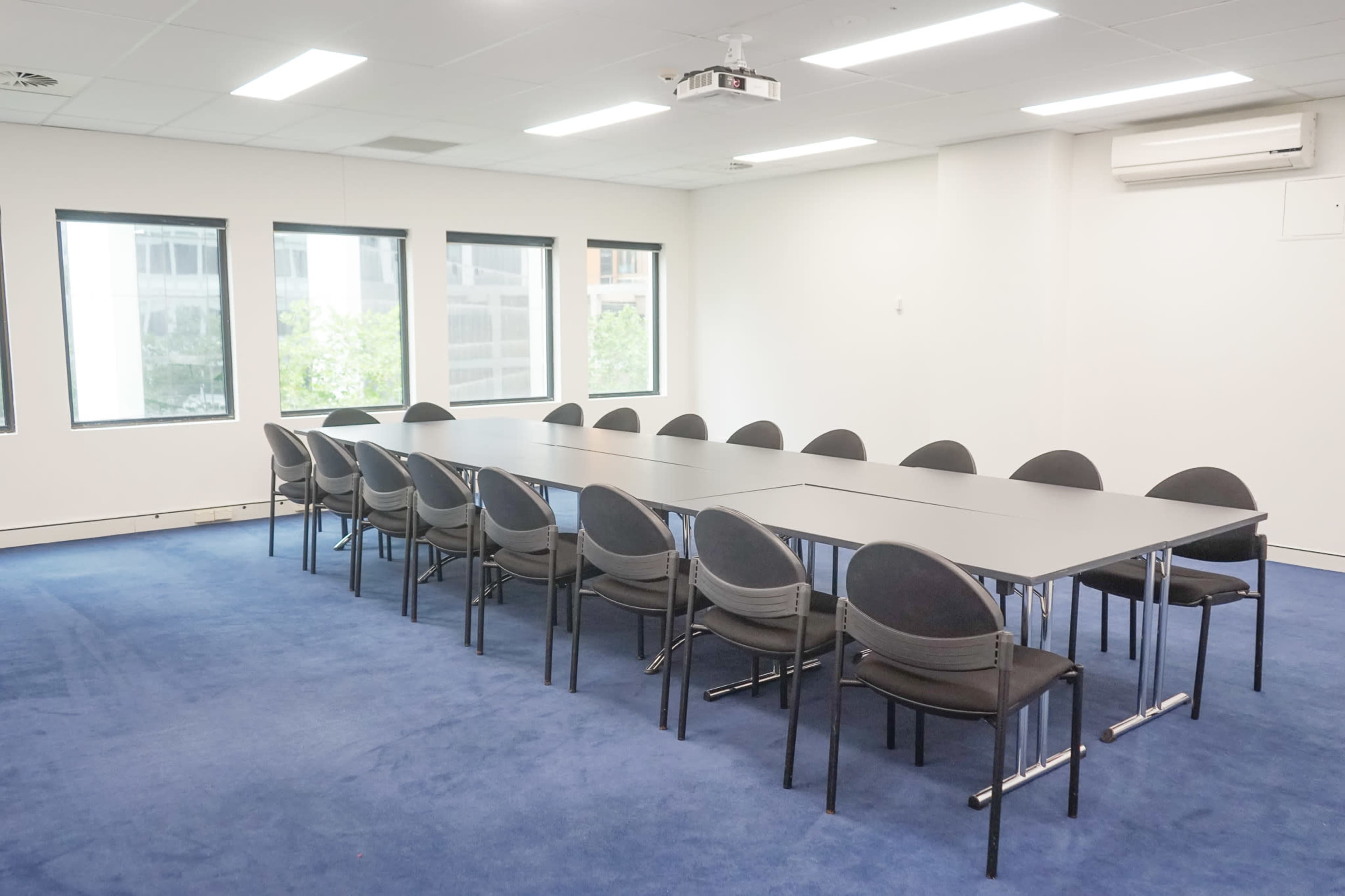 A conference room features a long table surrounded by chairs on a blue carpet.