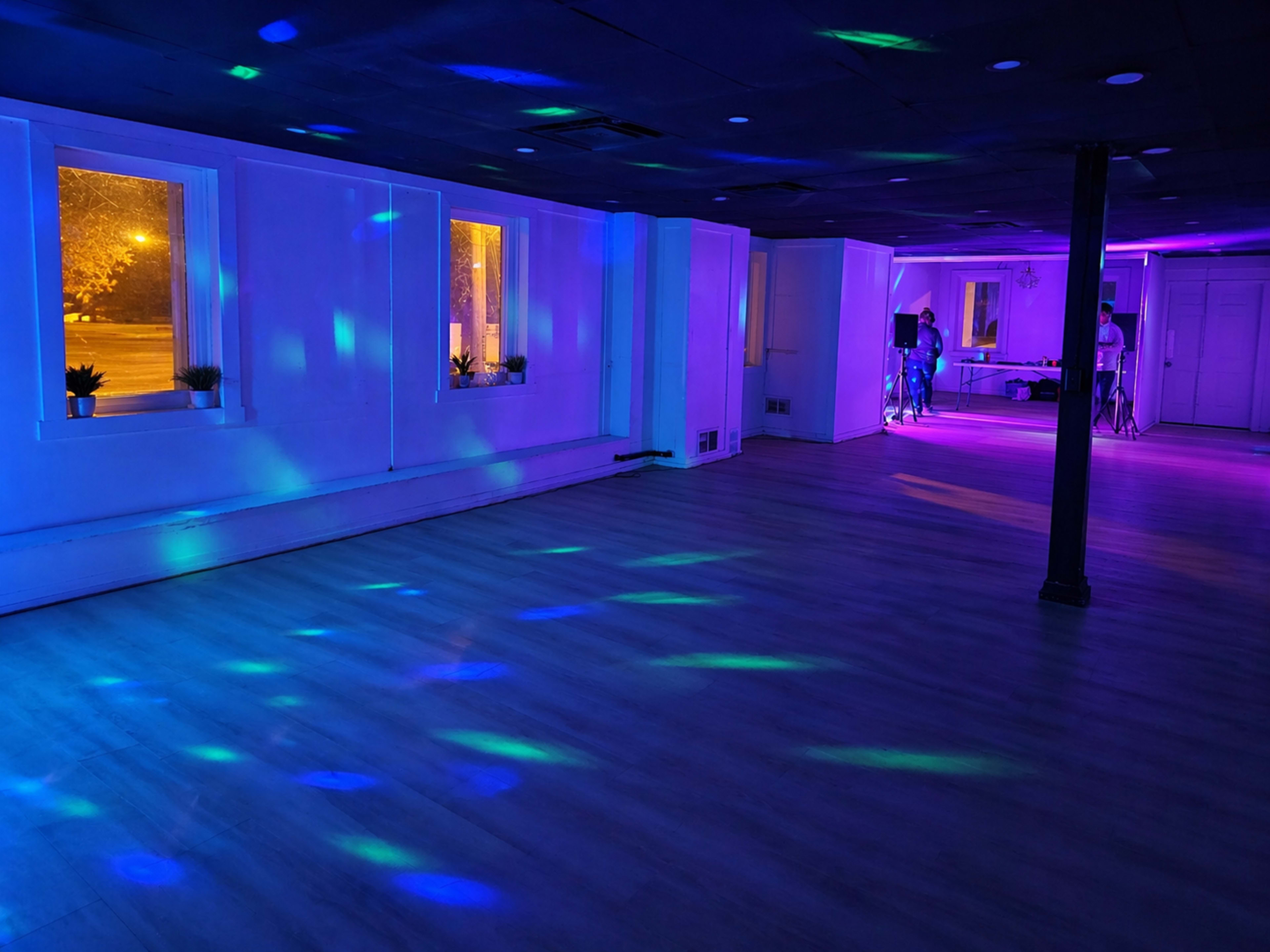 The image shows a spacious, empty room with colorful lights casting patterns on the floor and walls, and windows revealing a snowy scene outside.