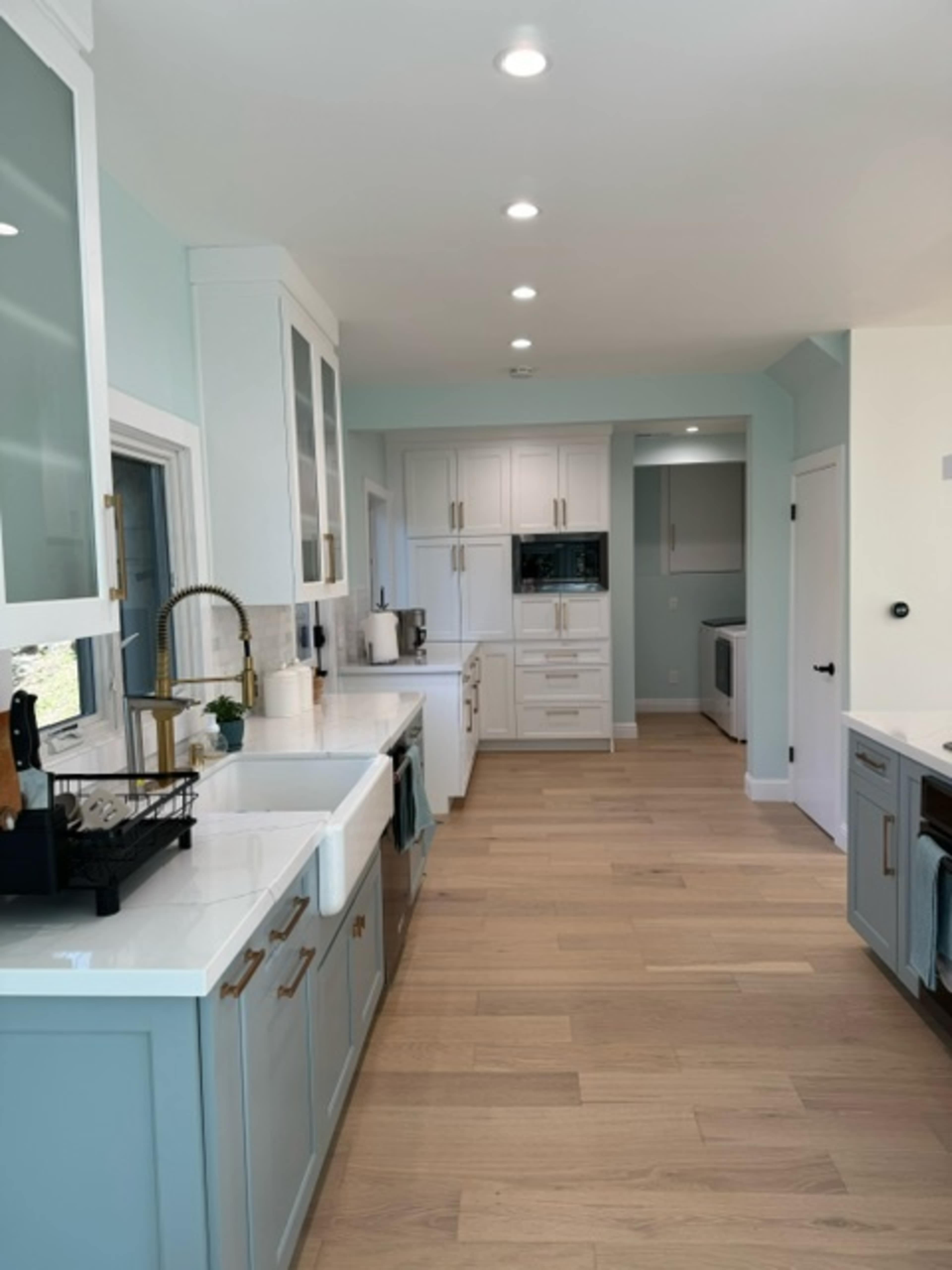 A modern kitchen with light-colored cabinets, a large sink with a faucet, and a spacious layout featuring hardwood flooring and ample natural light.