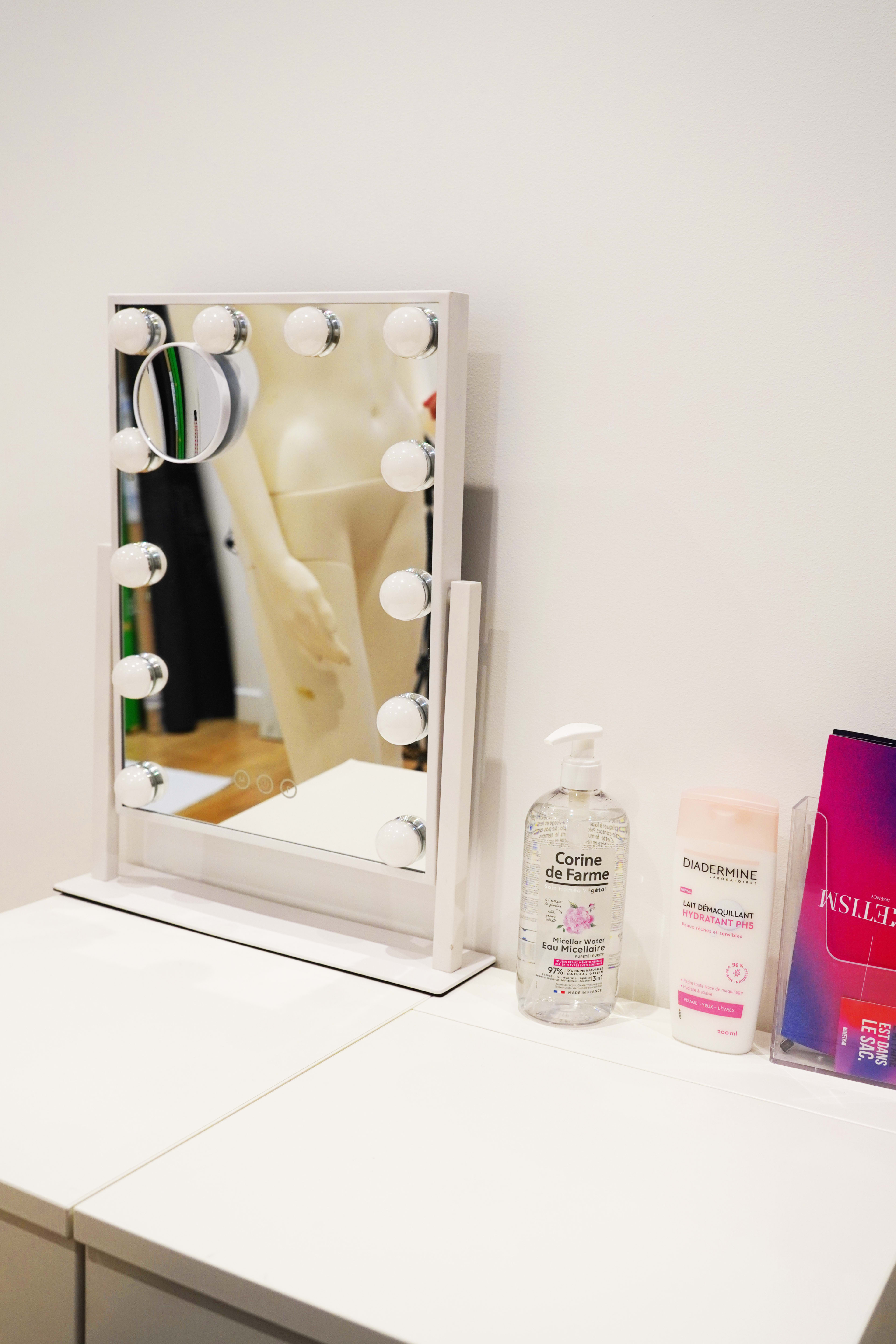A lighted makeup mirror is positioned on a white dresser next to skincare products.
