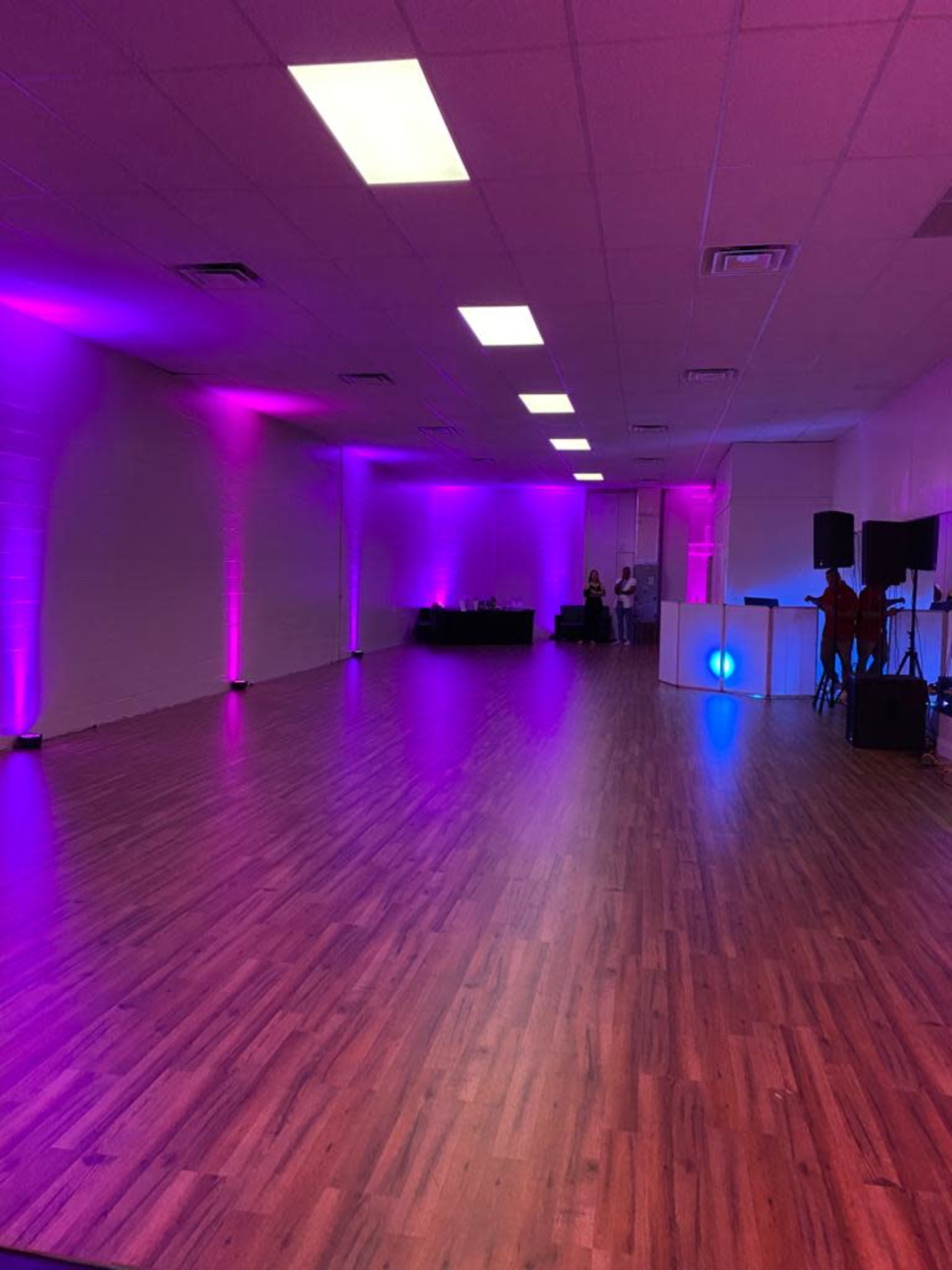 A spacious, well-lit room with a polished wooden floor and purple and blue lighting along the walls.