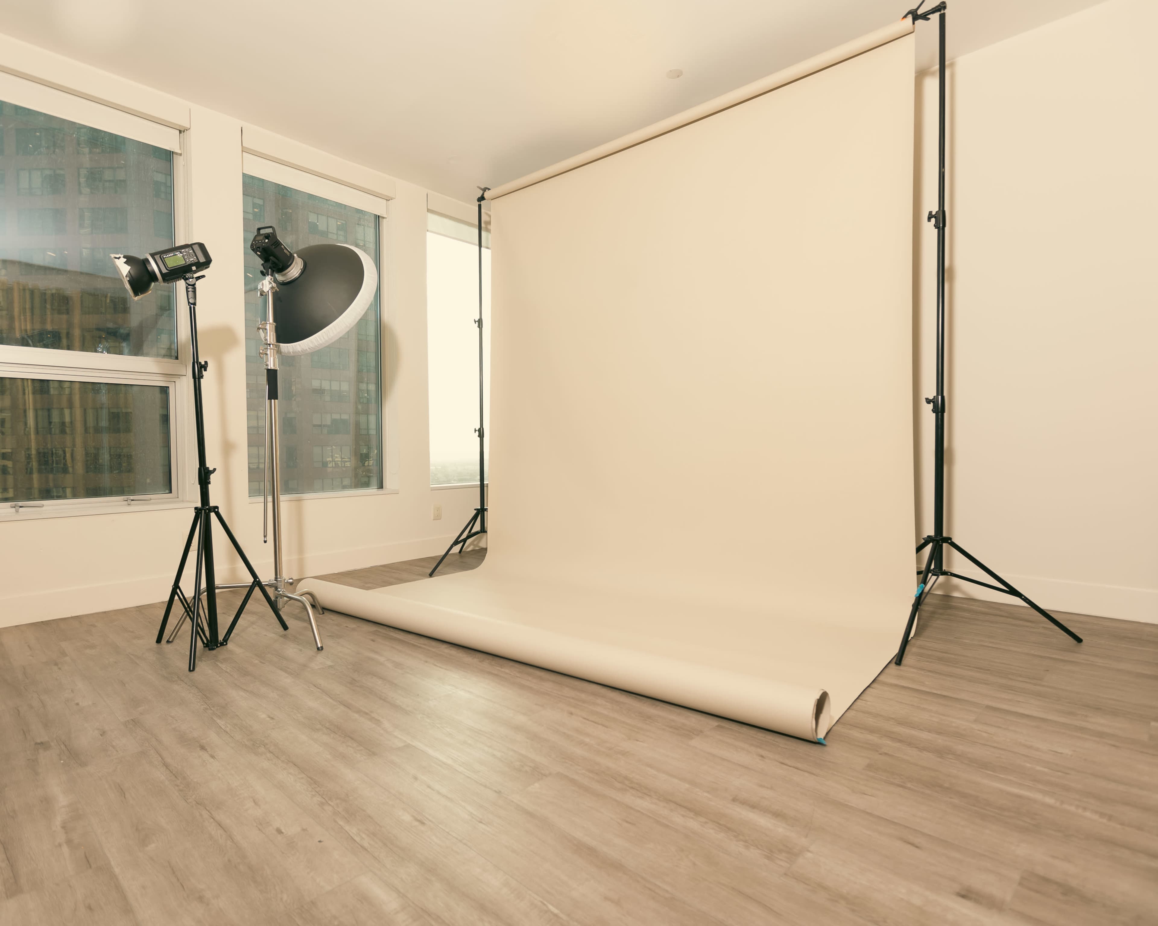 A photography studio setup with a light stand, a softbox, and a beige backdrop on the floor.