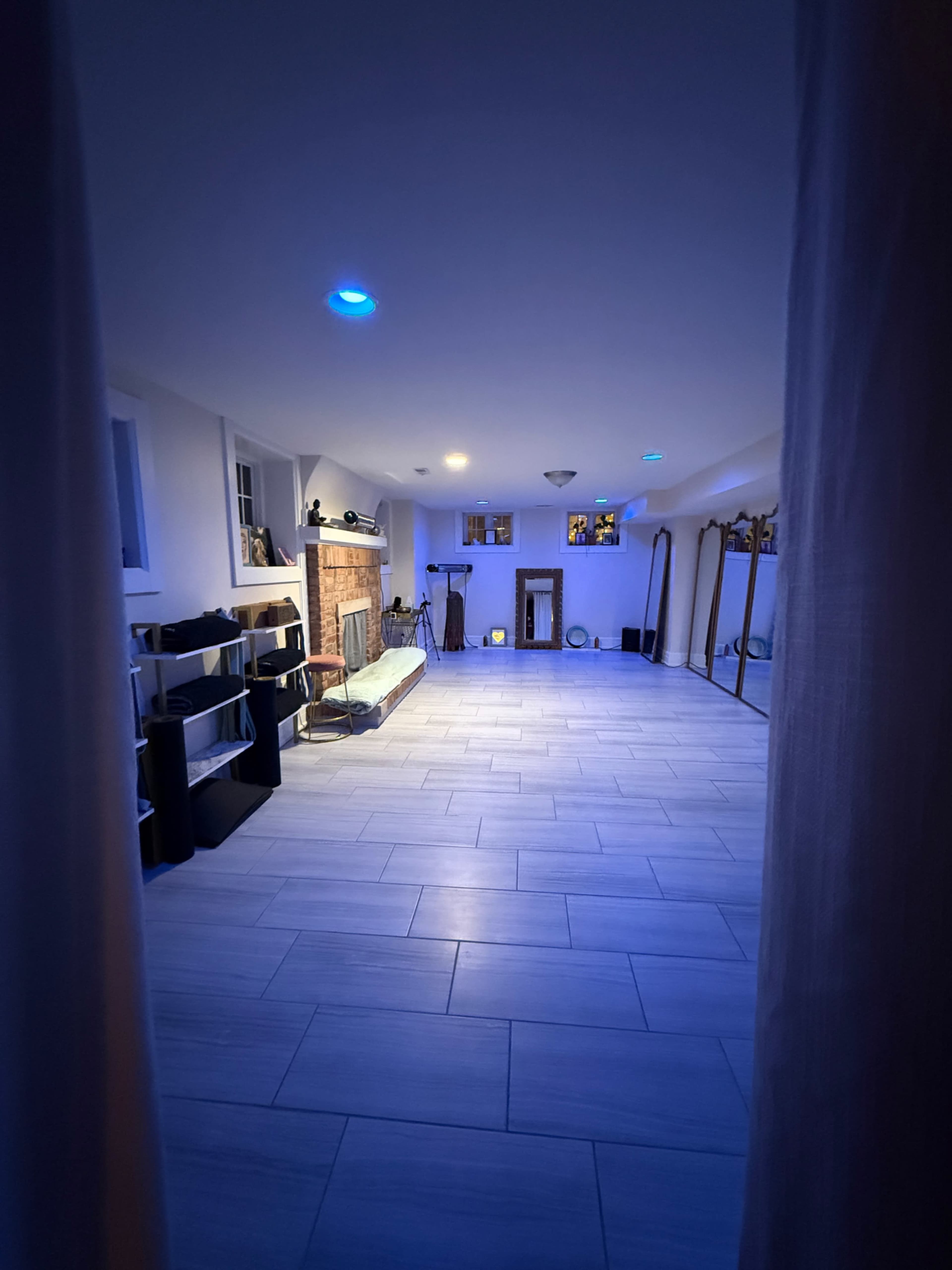The image shows a spacious, well-lit room with a fireplace, multiple mirrors, and shelves, all arranged neatly on a tiled floor.