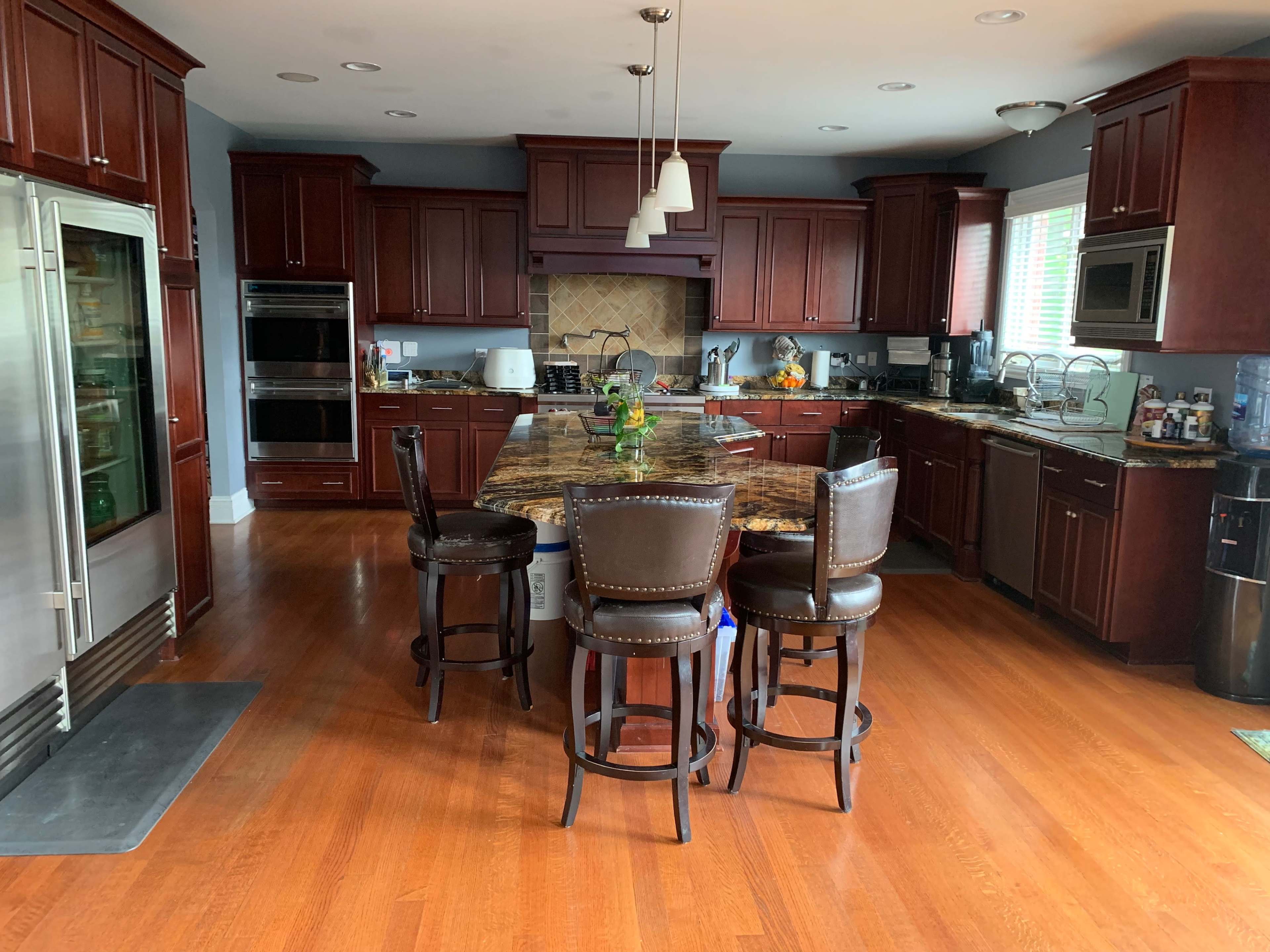 A modern kitchen features dark wooden cabinets, a large granite island with stools, and stainless steel appliances.