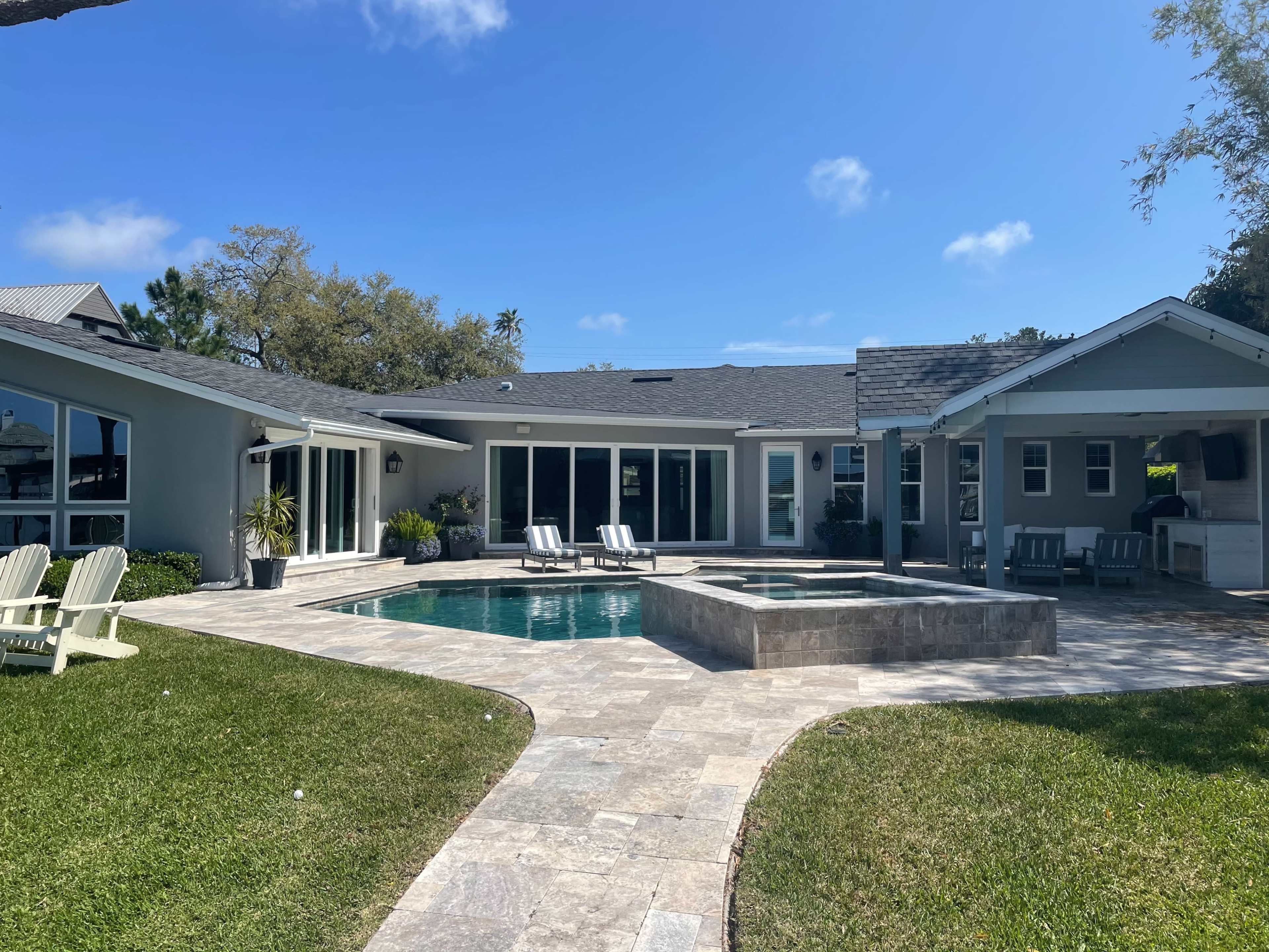 A modern house with a swimming pool and a stone patio surrounded by green grass and trees.