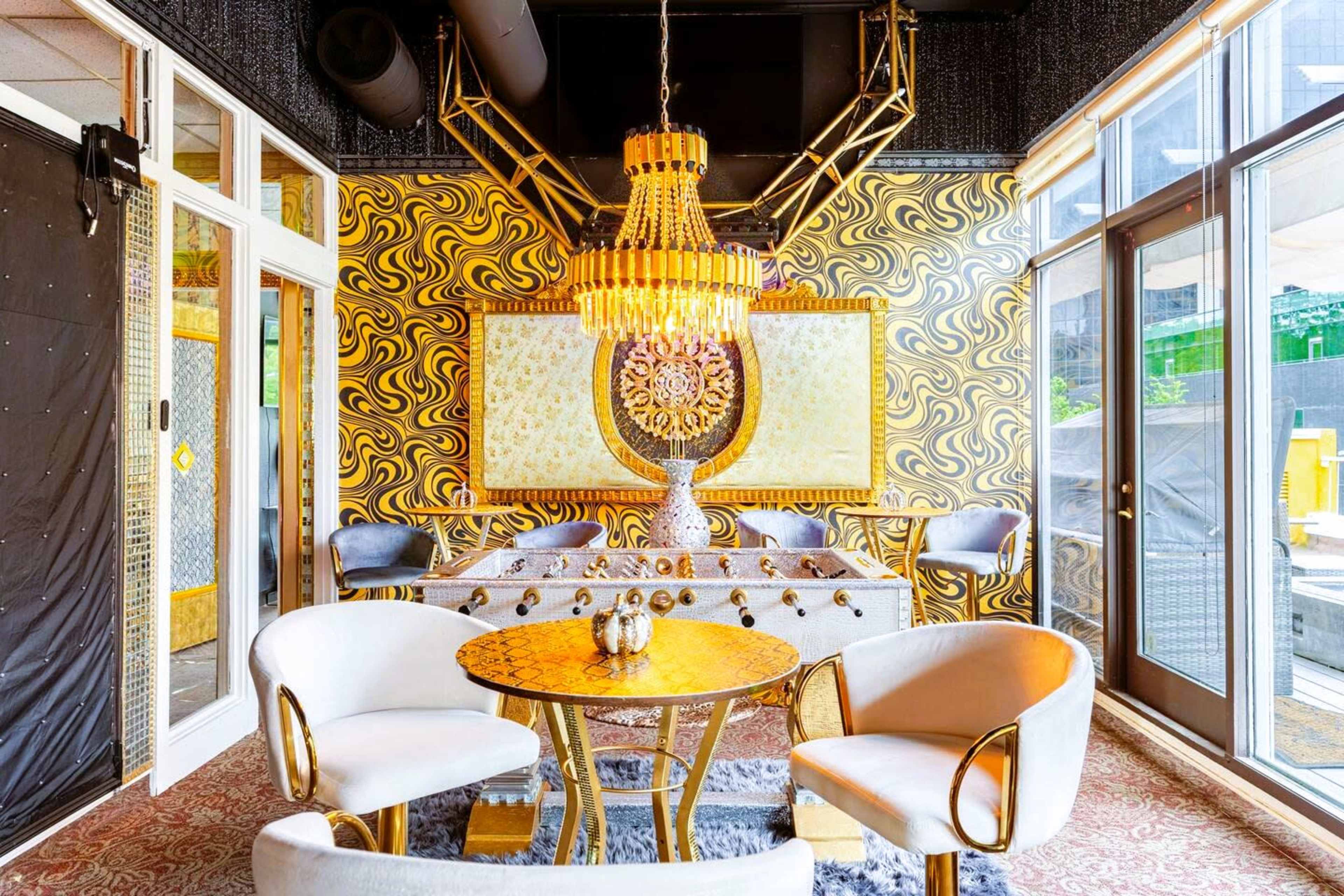 The image shows a stylish interior of a room featuring a round table with four chairs, a decorative chandelier, and a bold, patterned wall design.