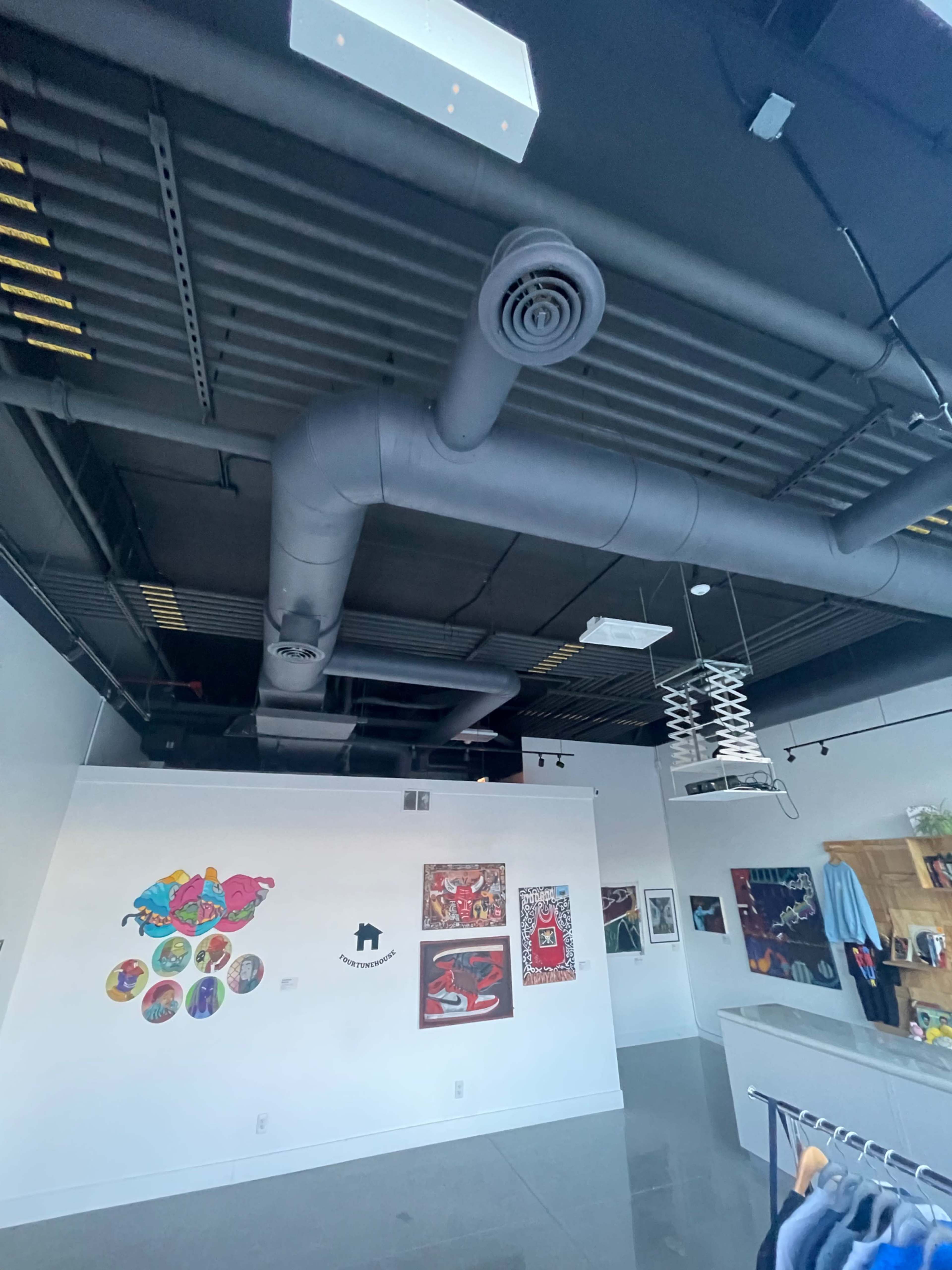 A modern retail space with exposed ductwork on the ceiling and various artworks displayed on the walls.