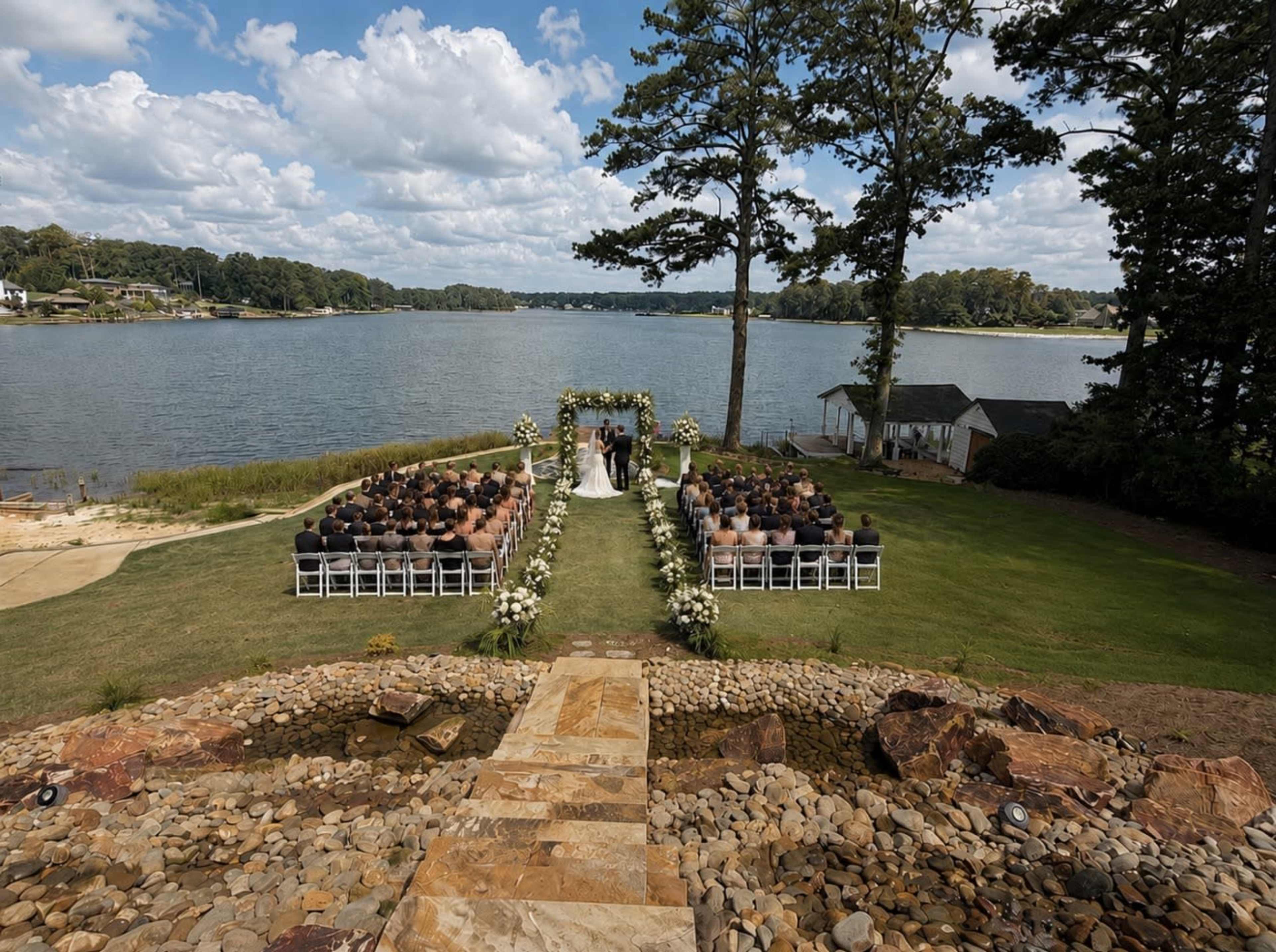 A wedding ceremony is set up by a lake, with rows of chairs facing an altar adorned with flowers and greenery.
