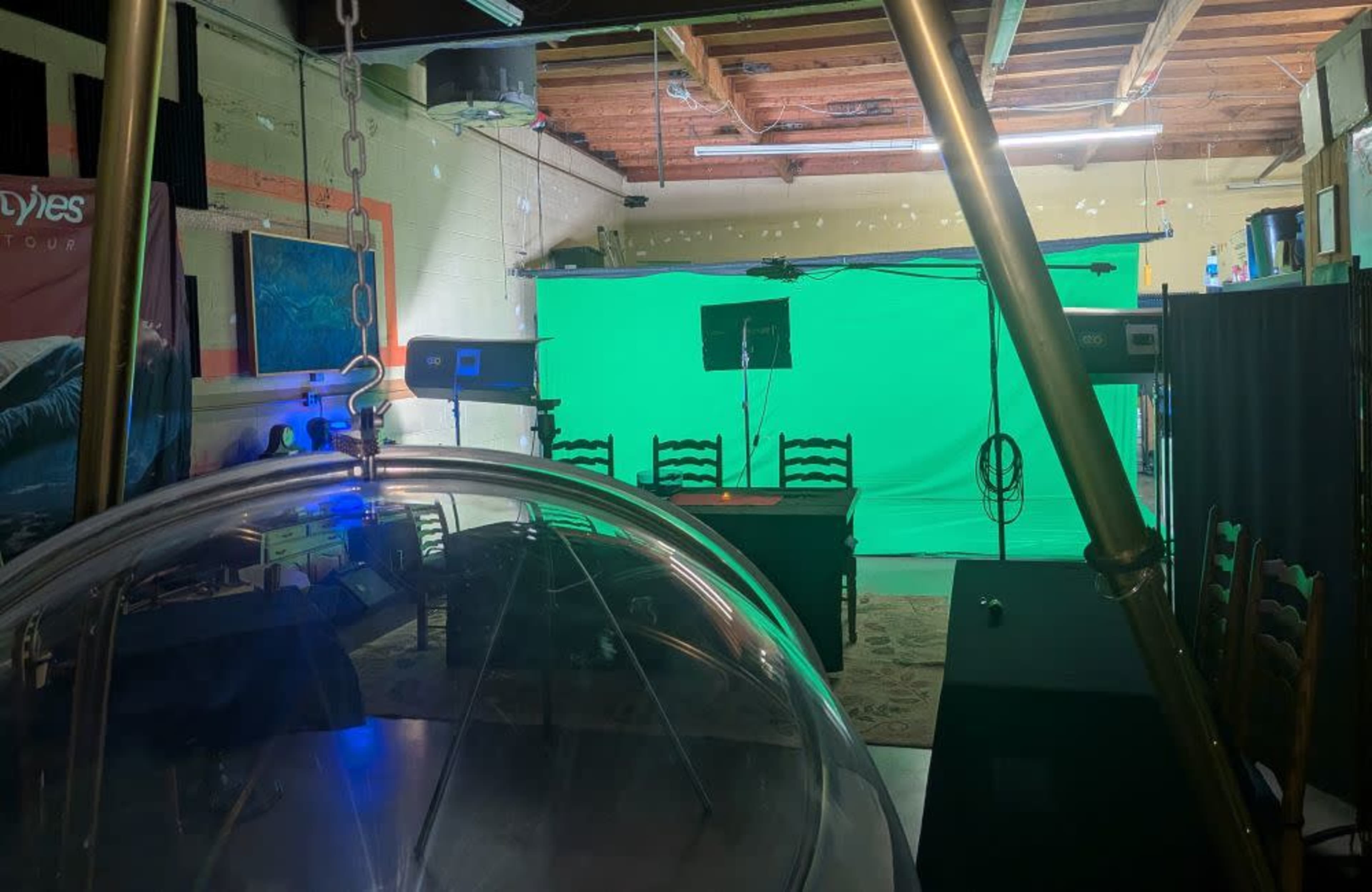 The image shows a studio setup with a green screen in the background, flanked by lighting equipment and chairs, with a large transparent dome in the foreground.