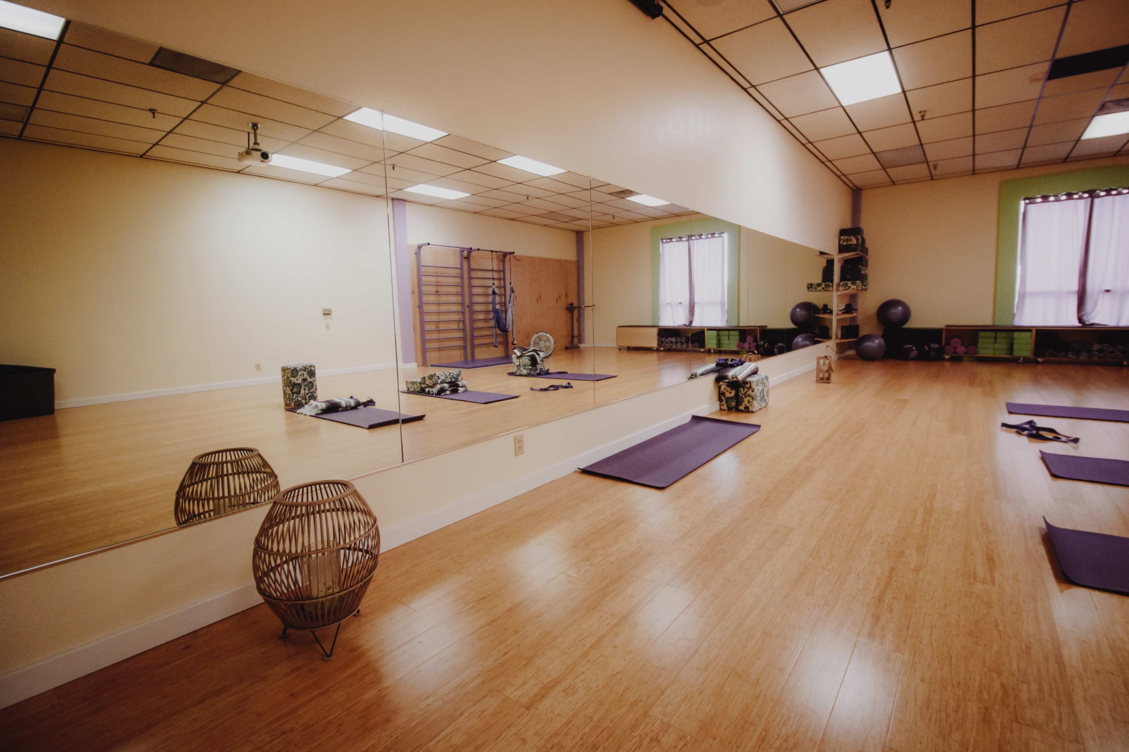 A spacious exercise studio features mirrored walls, yoga mats on the floor, and exercise equipment along one side.