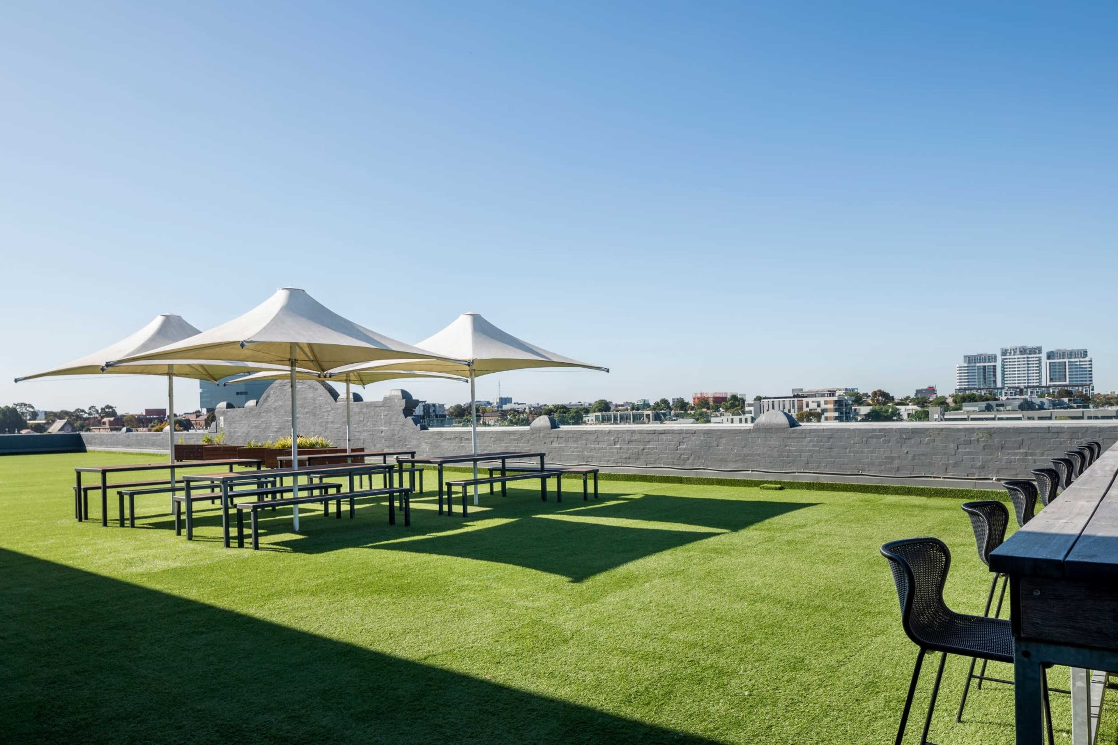 A rooftop area features several large tables under white canopies, set against a backdrop of a clear blue sky and distant city buildings.