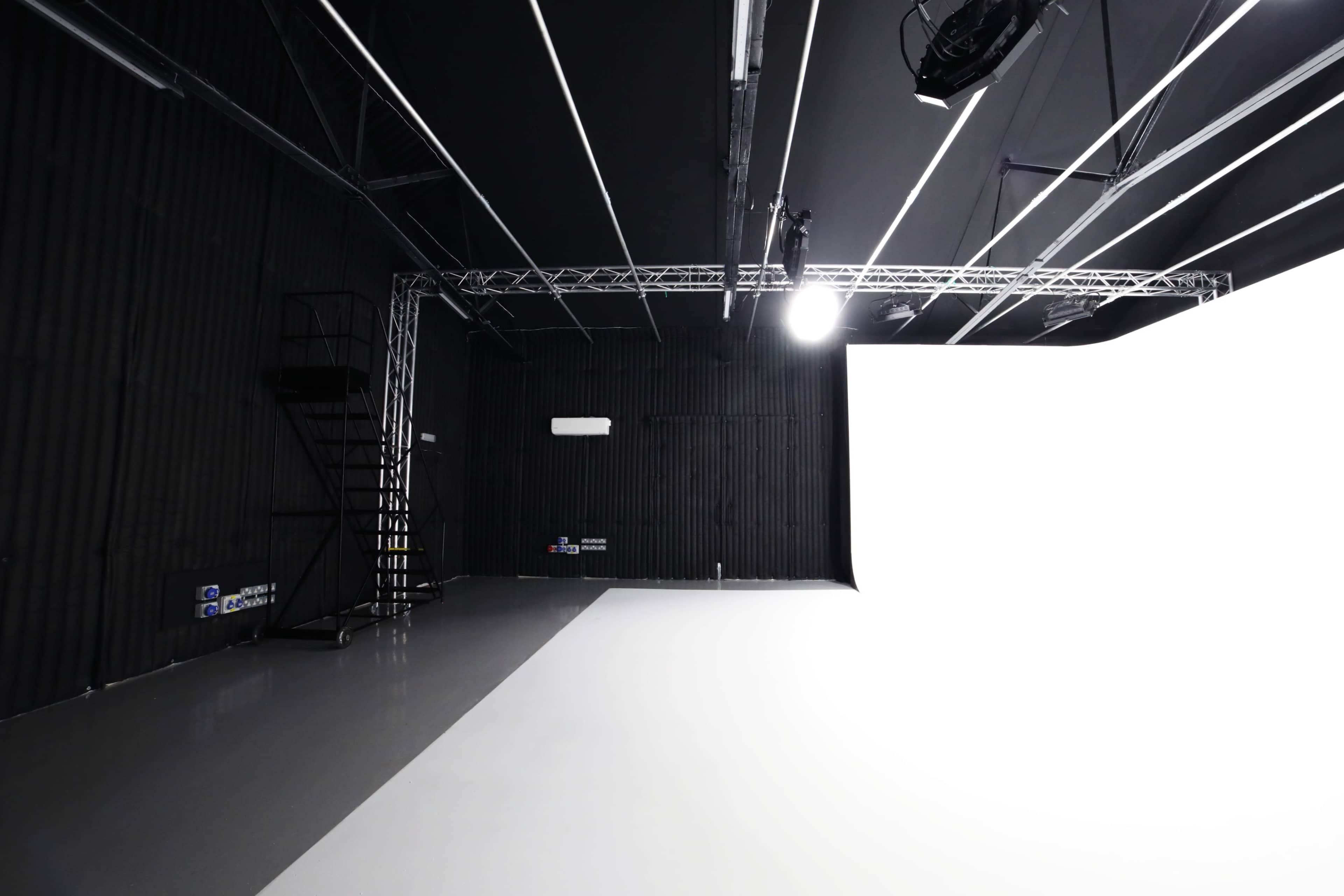 A minimalist studio space with a predominantly white backdrop, black walls, and a staircase in the corner.