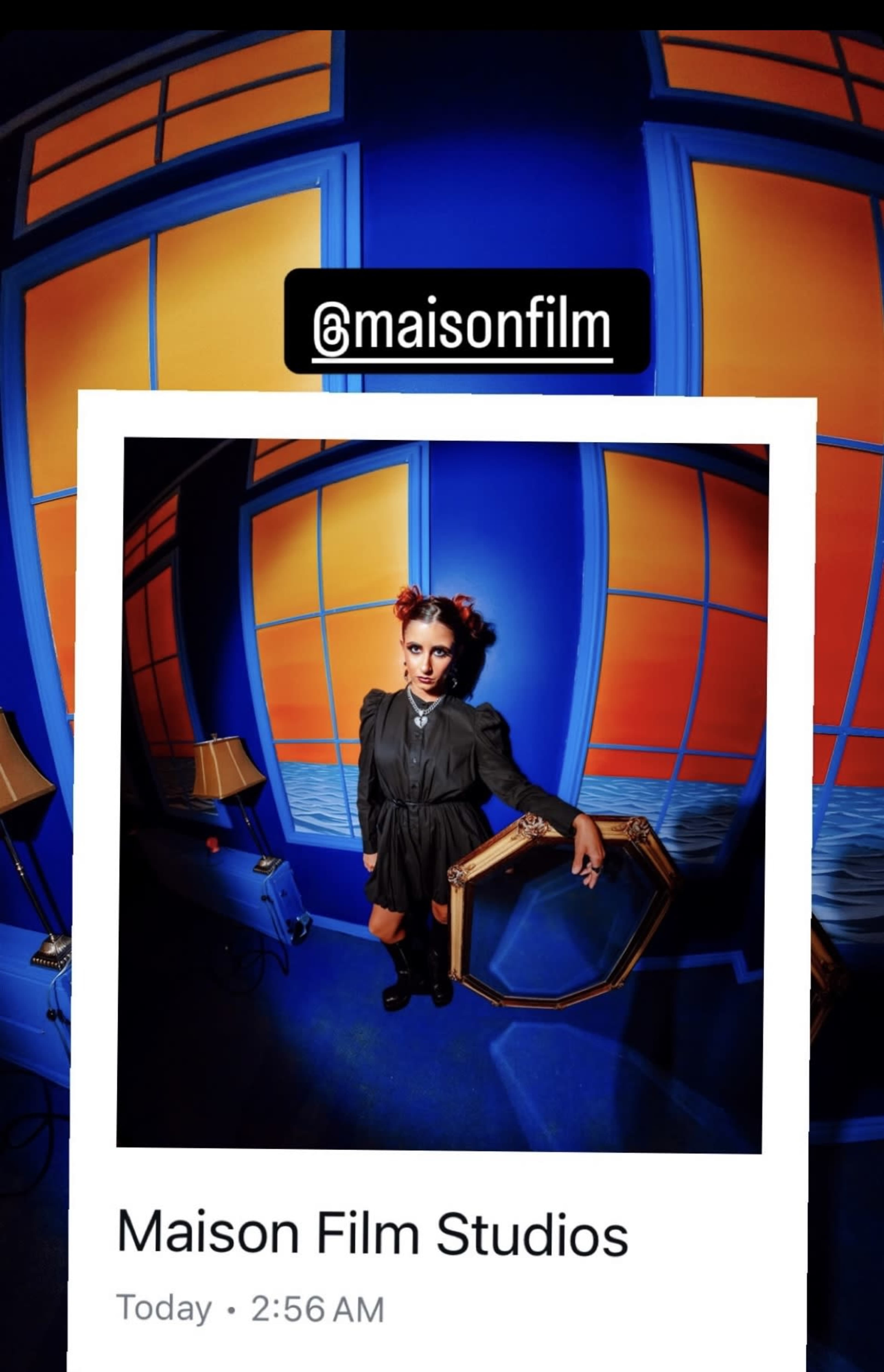 A person in a dark outfit poses in front of a brightly colored blue and orange background at Maison Film Studios.