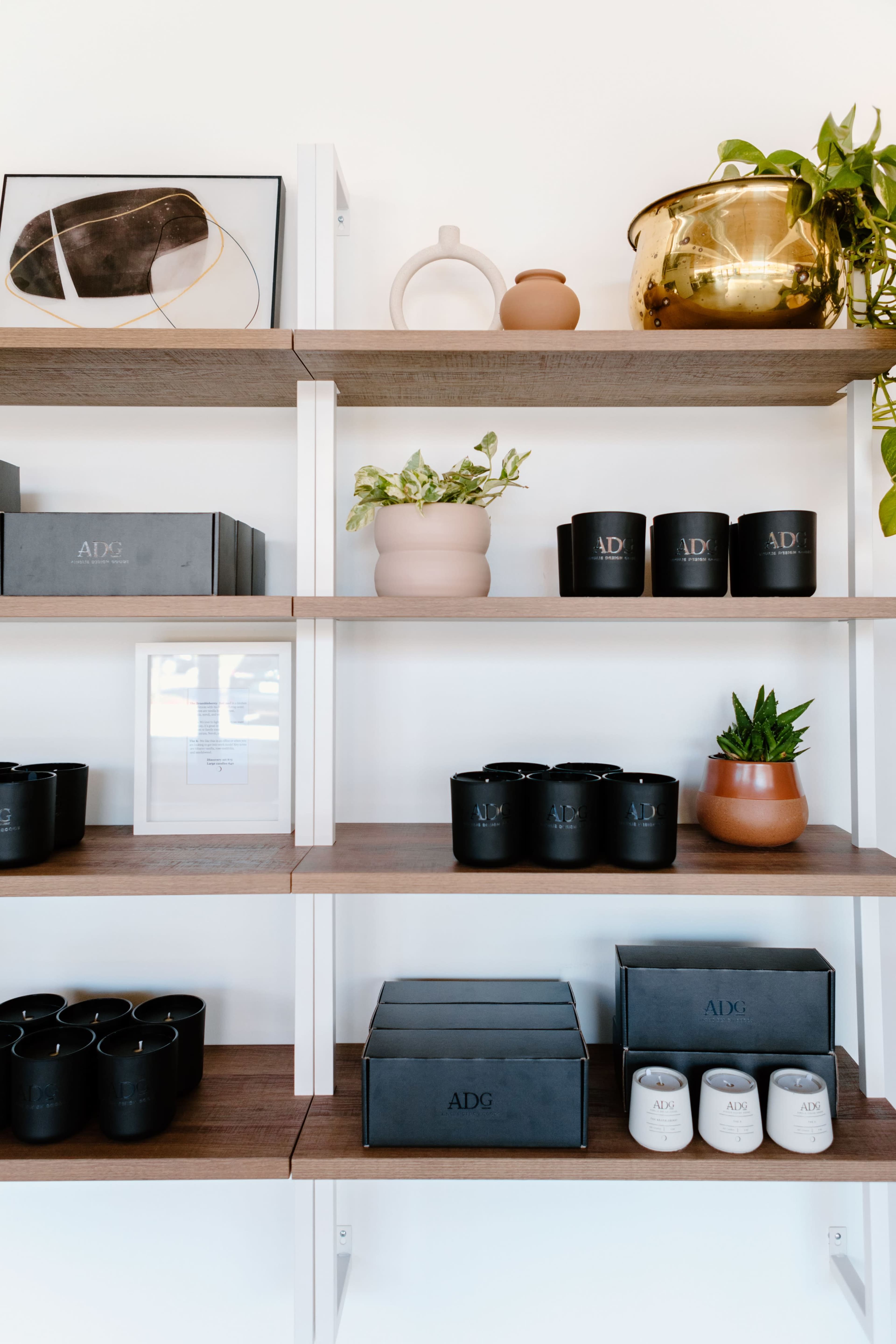 A wooden shelf displays various decorative items, including candles in black containers, a potted plant, and other ceramic pieces.