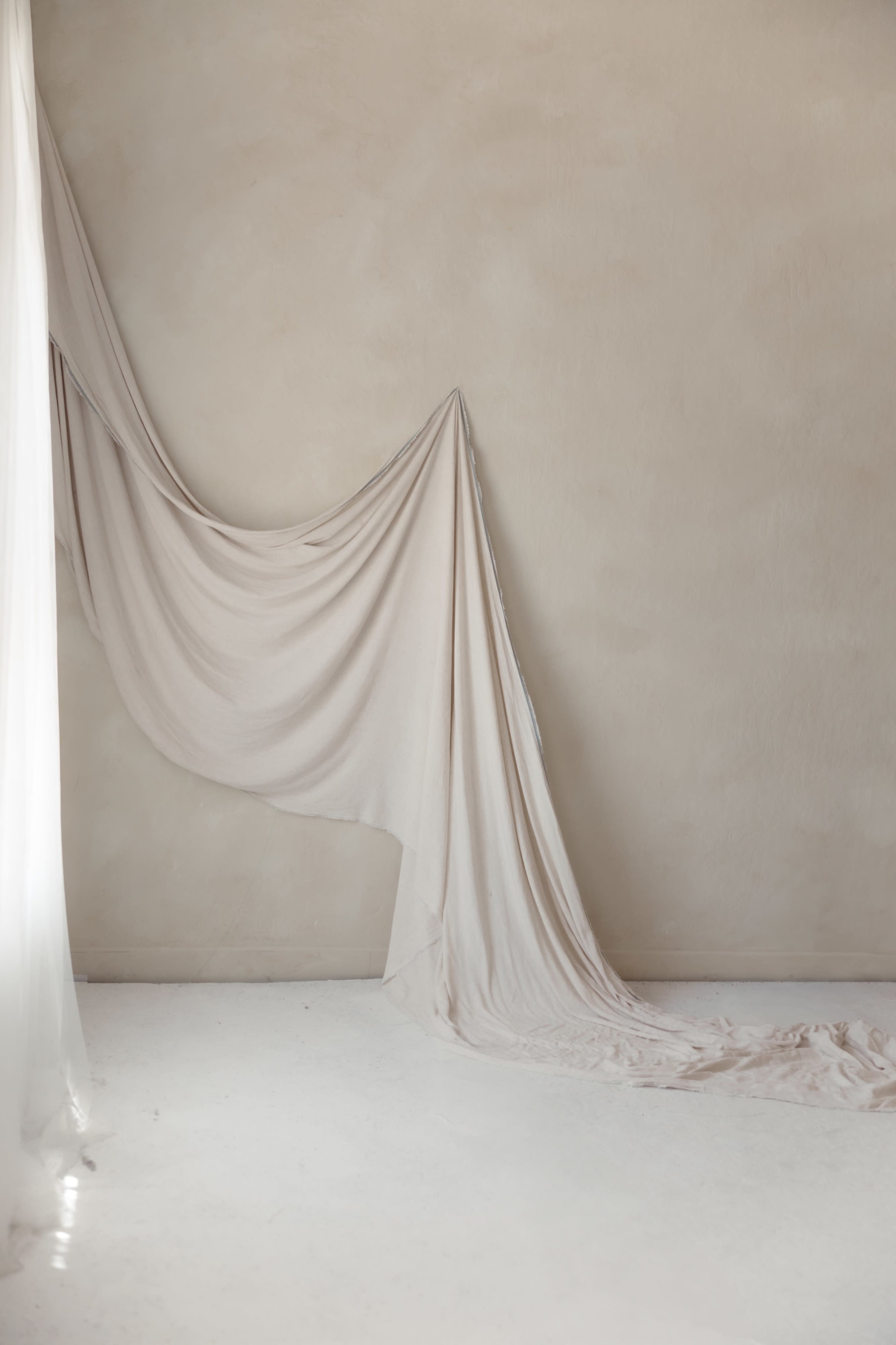 A large piece of draped fabric hangs against a smooth, neutral-colored wall, with one end cascading to the floor.