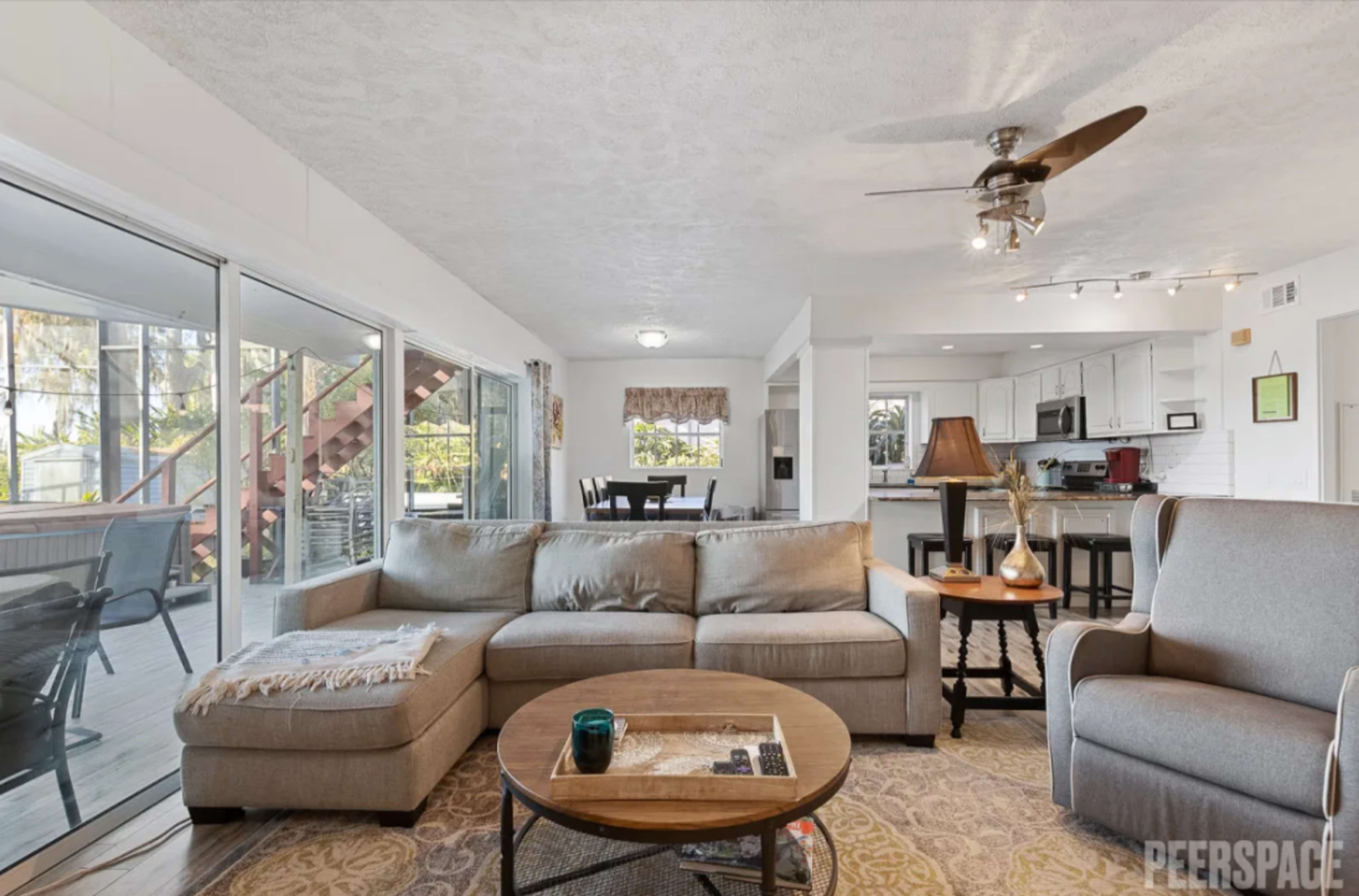 A light-filled living room featuring a large sectional sofa, a coffee table, and an open view into the kitchen and dining area.