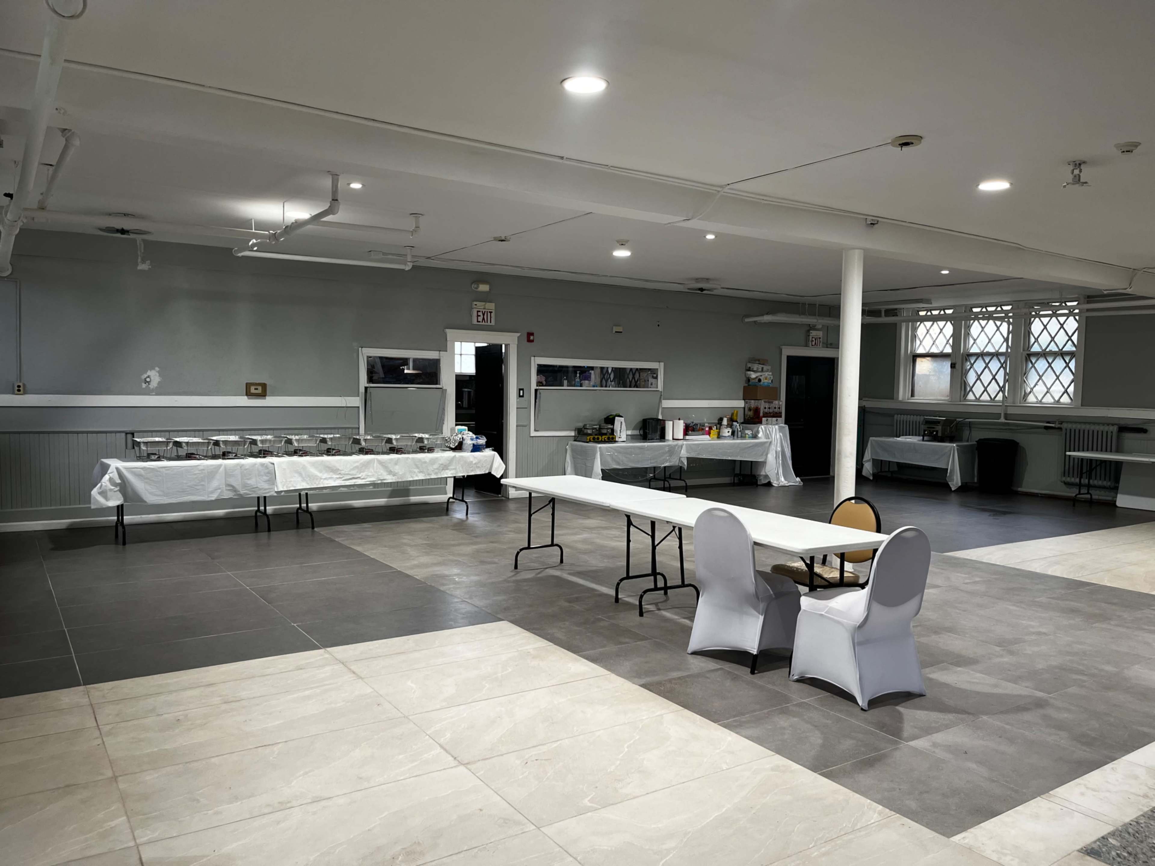 A spacious indoor venue with a long table set for a buffet and a small seating area featuring a table and two chairs.