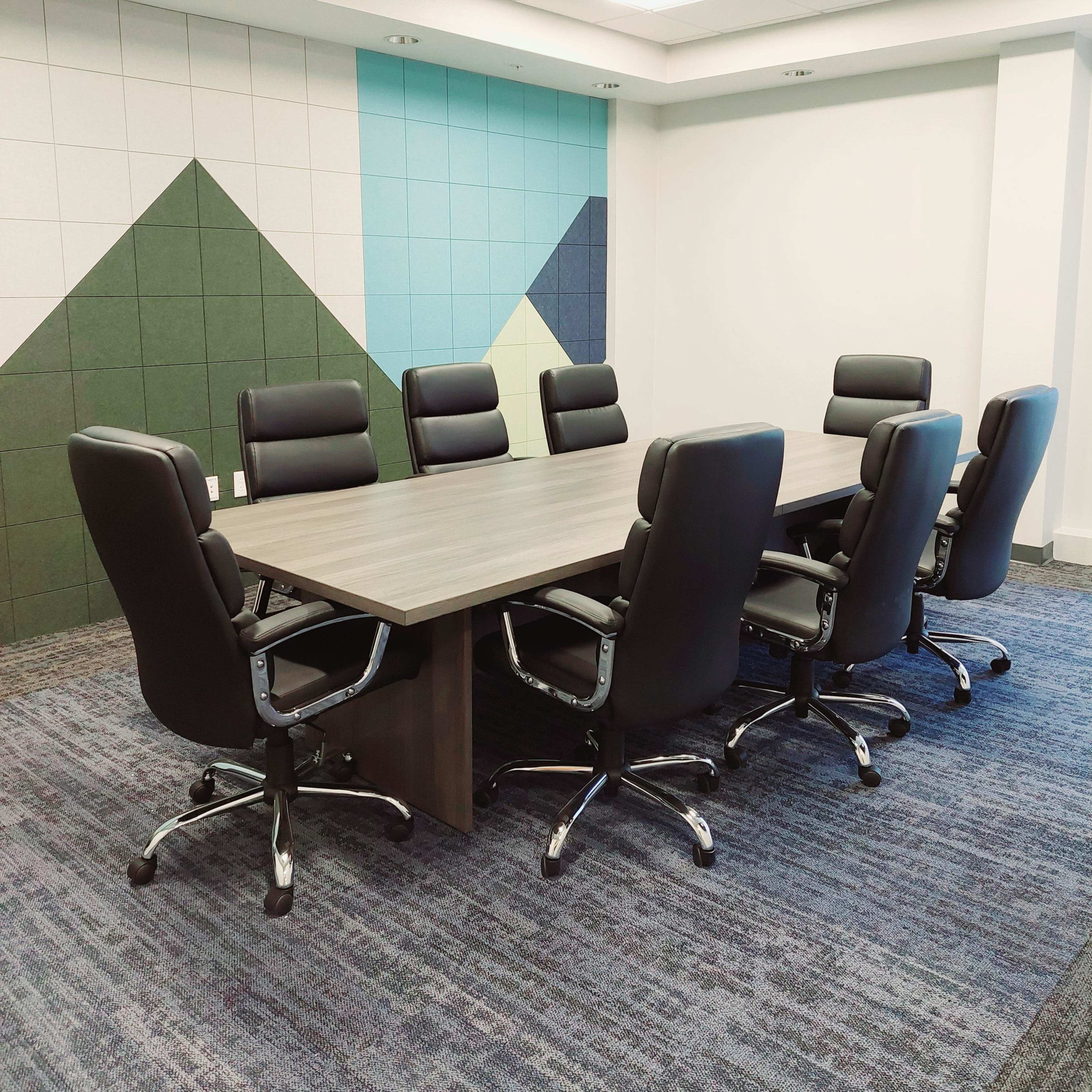 A modern conference room features a large table surrounded by eight black ergonomic chairs, set against a backdrop of colorful geometric wall designs.