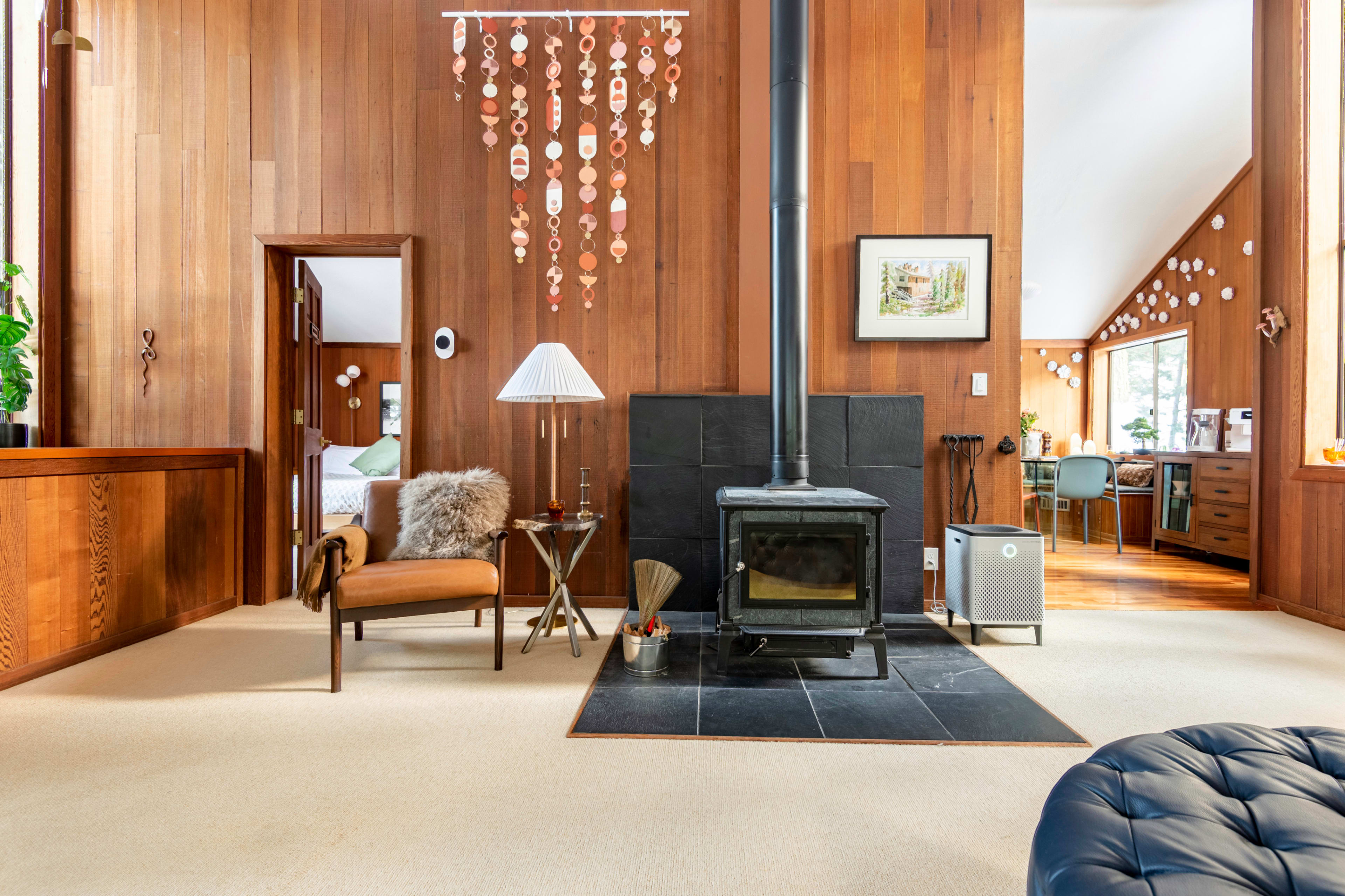 A cozy living area featuring a wood-paneled wall, a wood stove, and a chair beside a lamp.