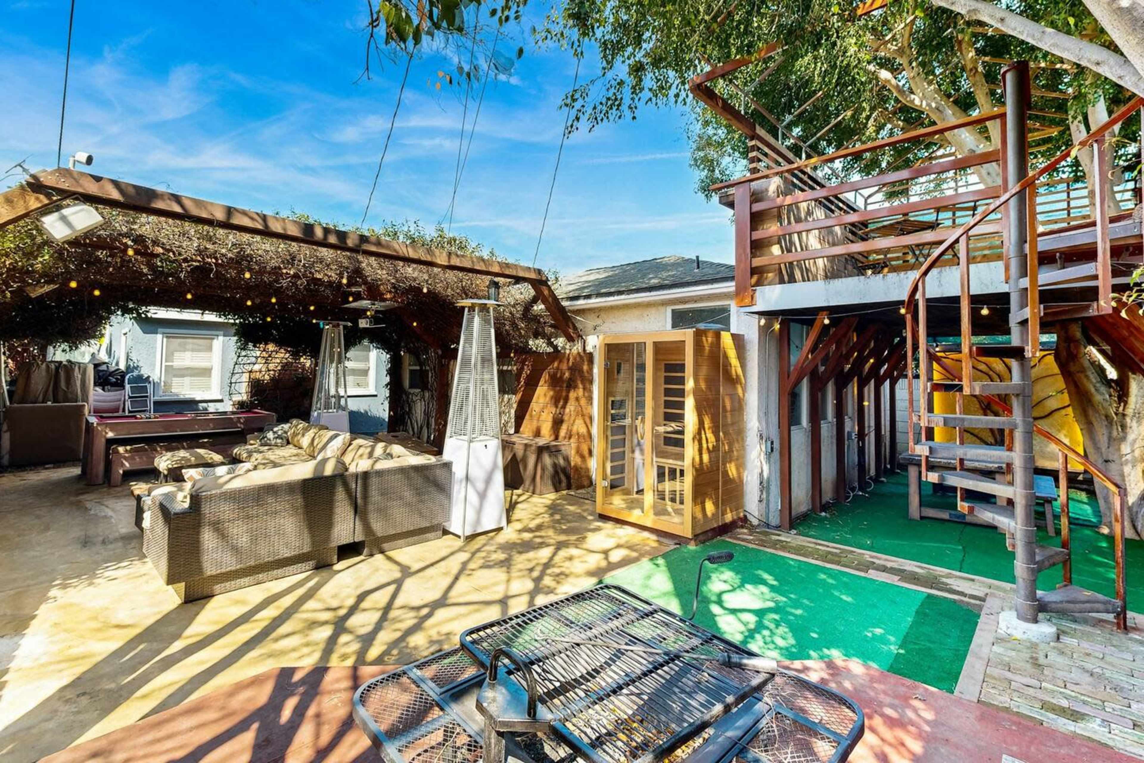 A patio area with outdoor seating, a spiral staircase leading to a deck, a wooden structure resembling a sauna, and decorative overhead lights.