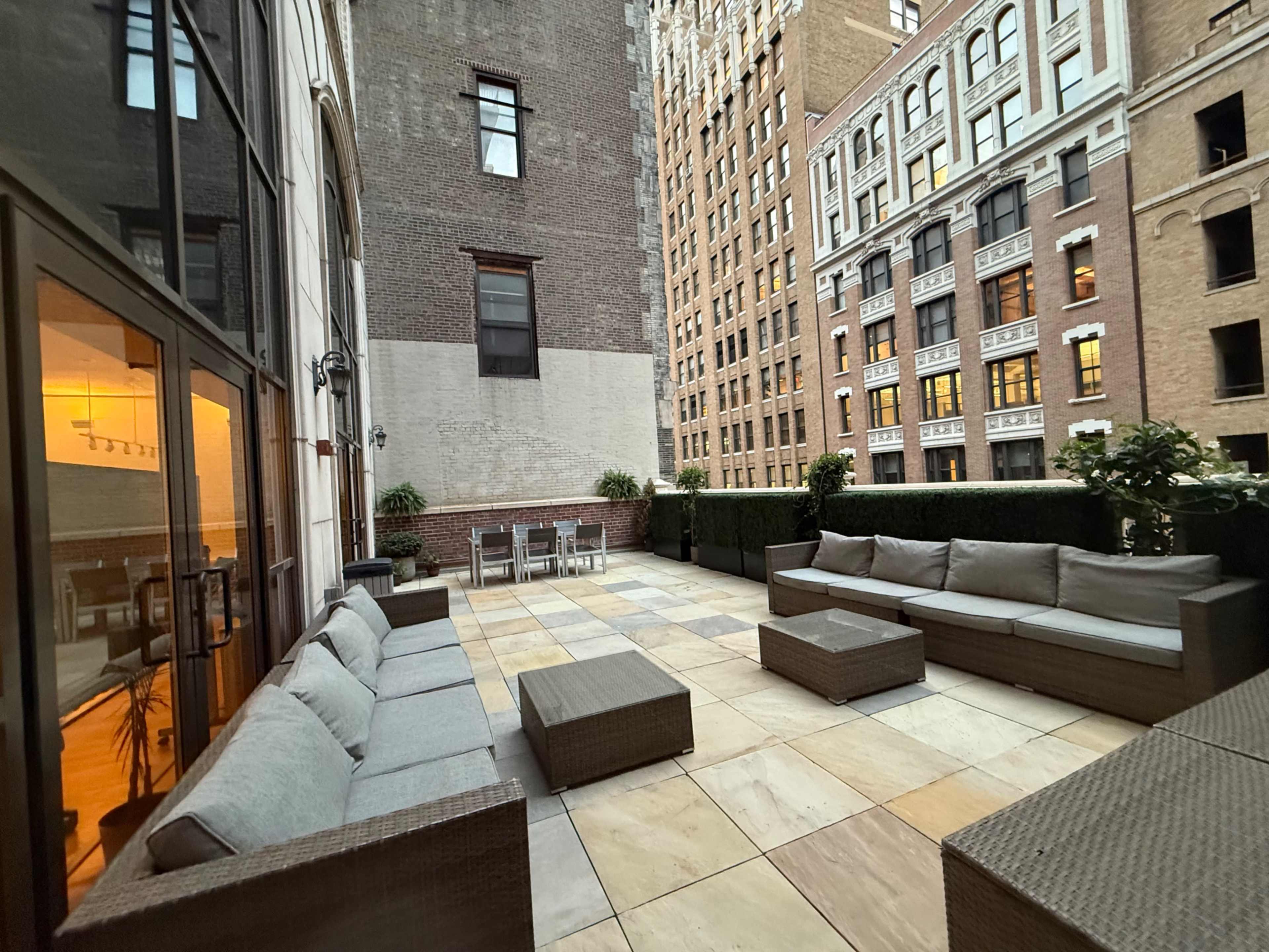 The image shows a spacious rooftop terrace with modern seating arrangements, surrounded by tall buildings.