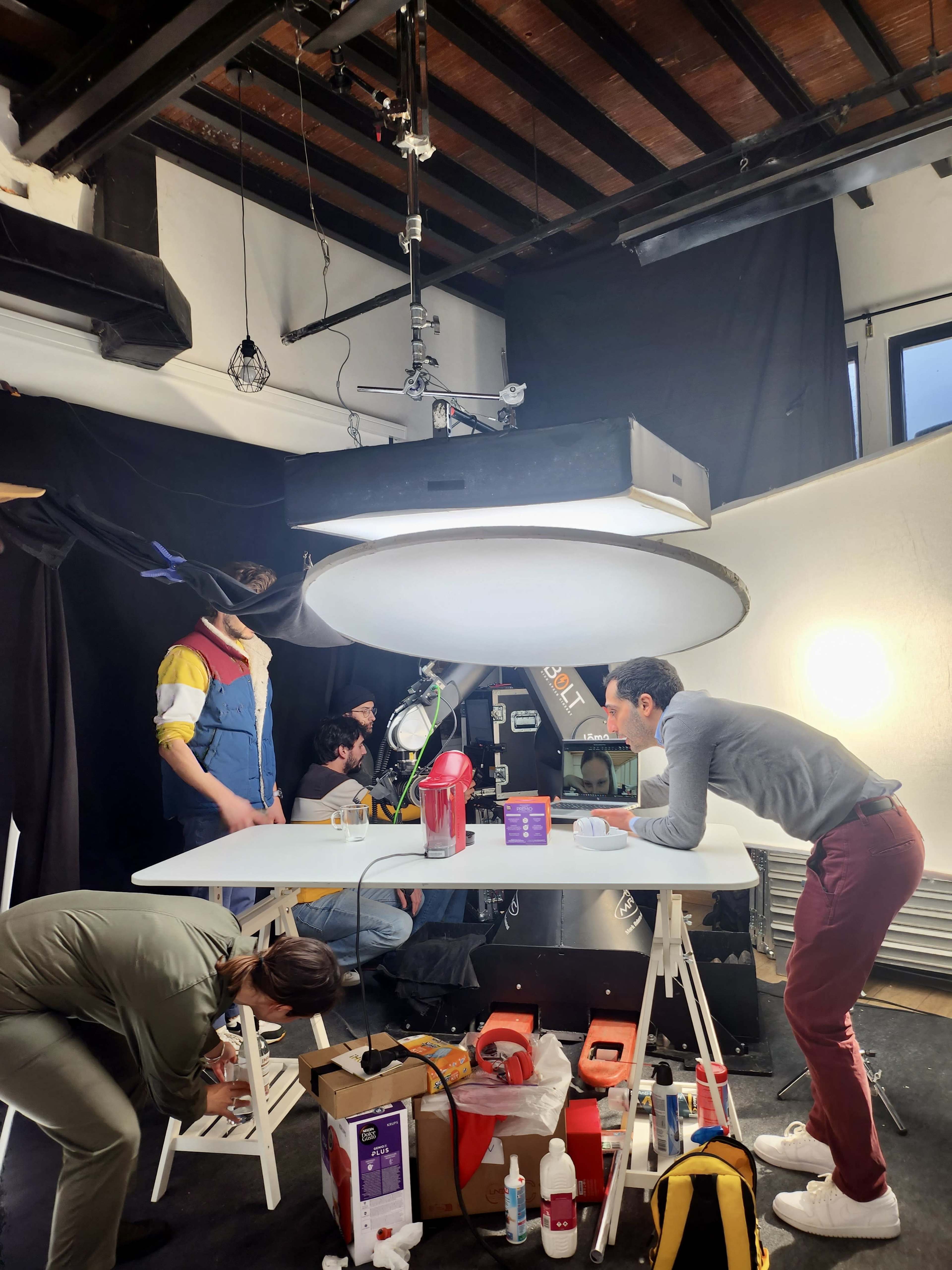 A group of five people is working in a studio setting with a large light above a table while setting up or preparing for a shoot.