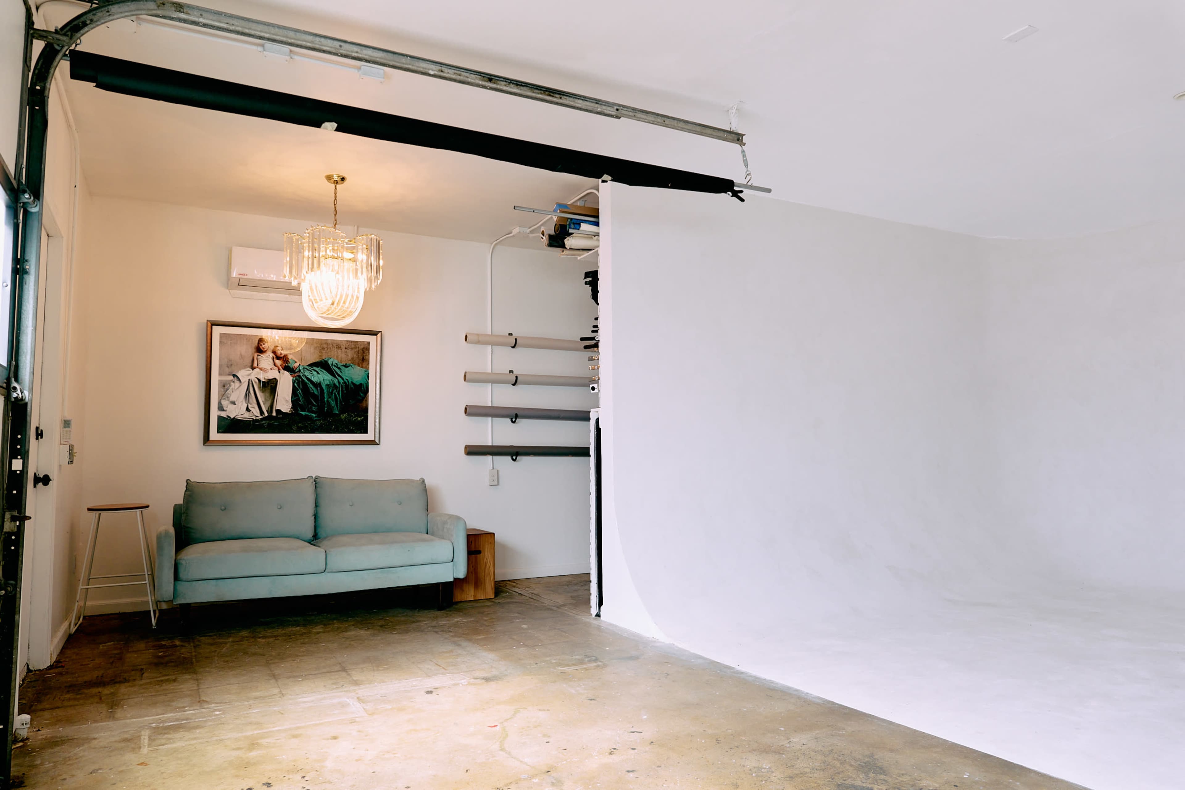The image shows an interior space featuring a light-colored backdrop, a blue sofa, a chandelier, and wall-mounted storage pipes.