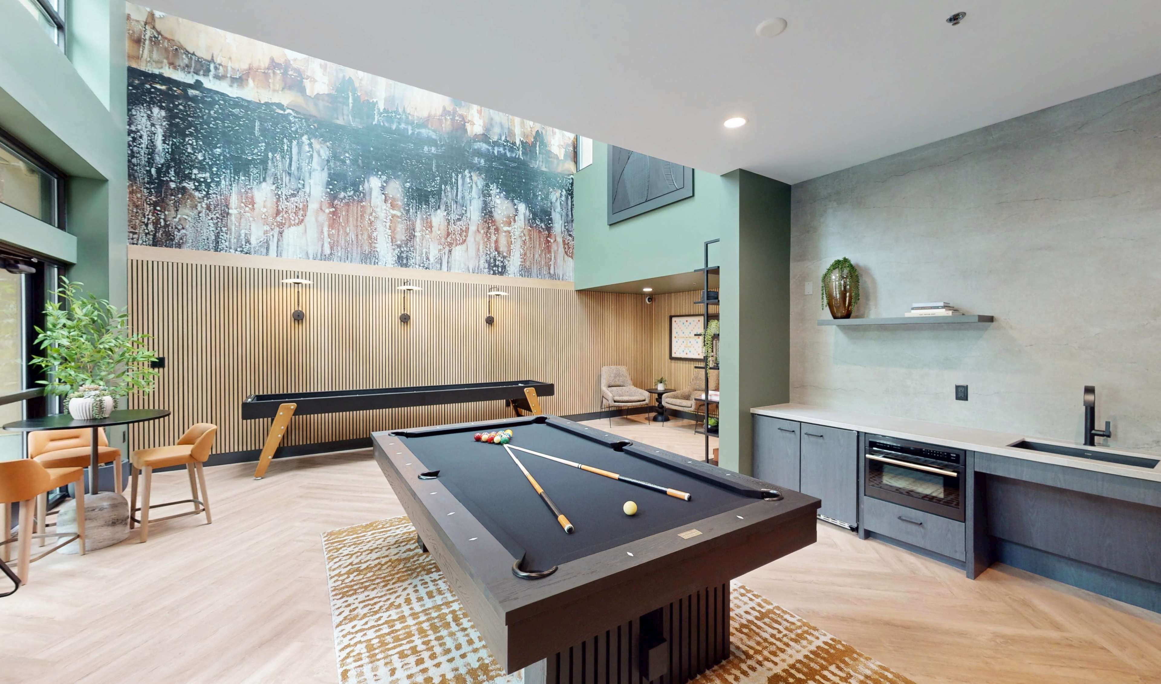 The image shows a modern game room featuring a billiards table, a lounge area, and a large mural on the wall.