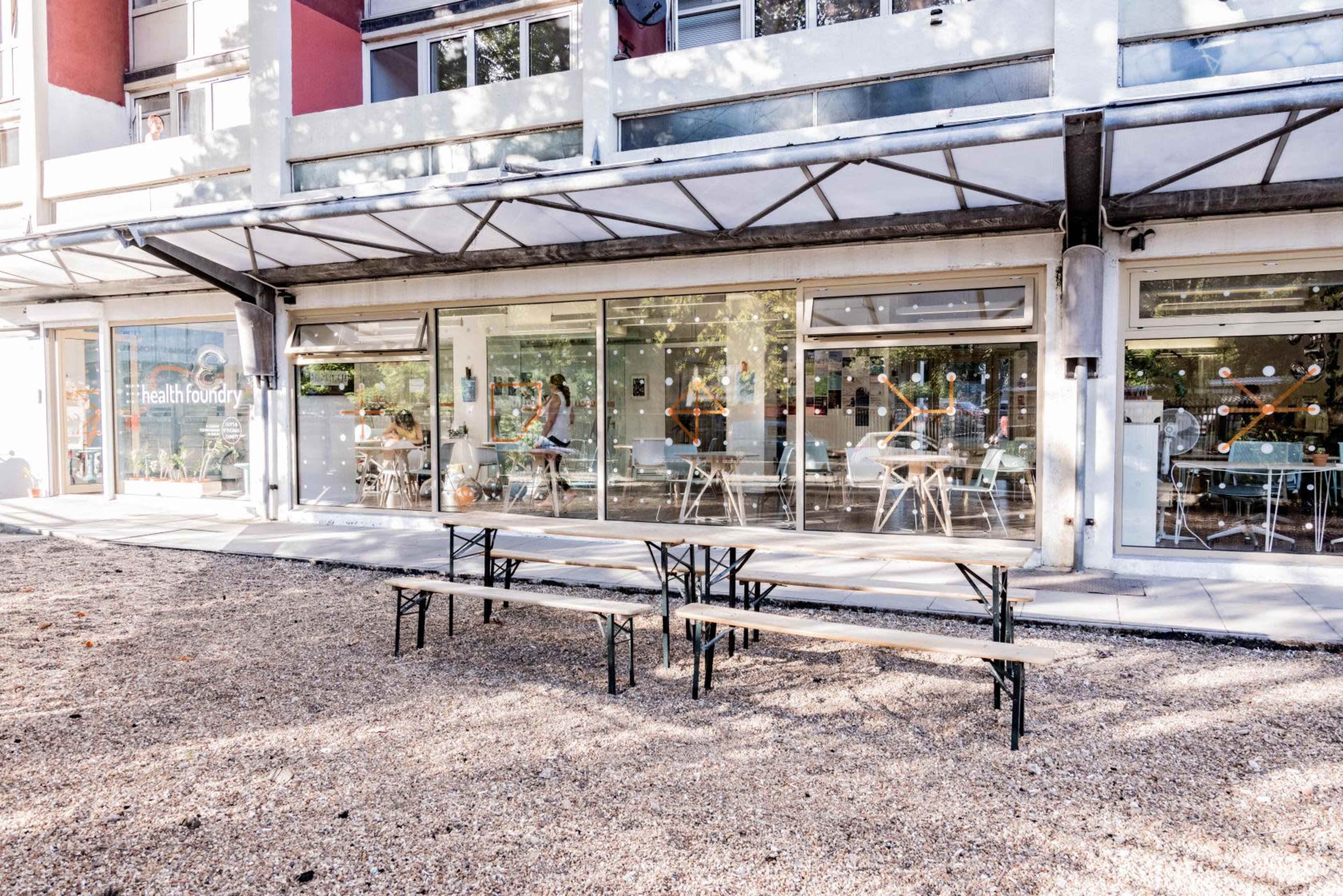 A modern café with large glass windows and outdoor seating area, situated under a covered patio and surrounded by a gravel surface.