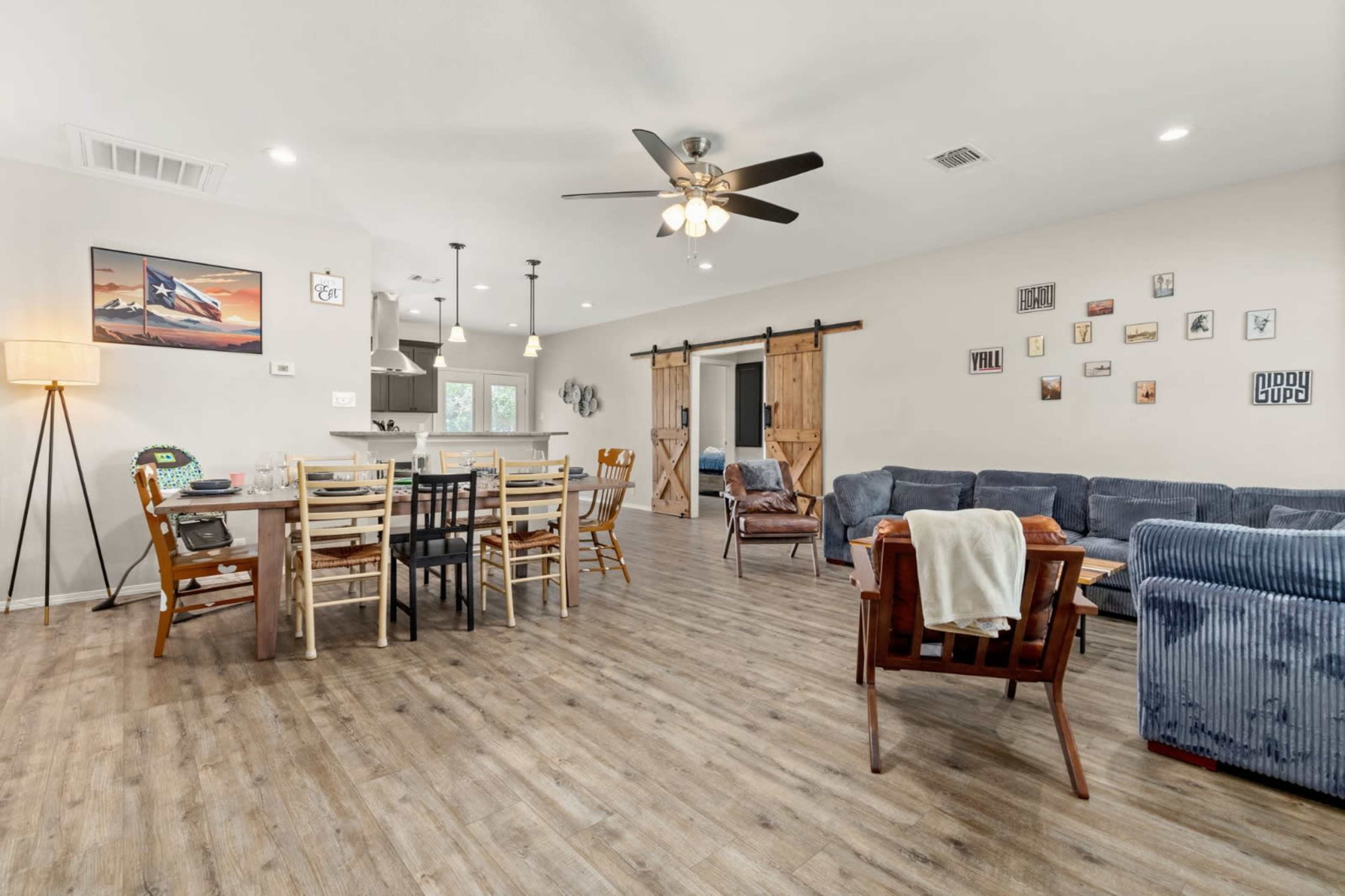 The image shows a spacious living and dining area with a wooden dining table, mixed seating arrangements, and sliding barn doors leading to another room.